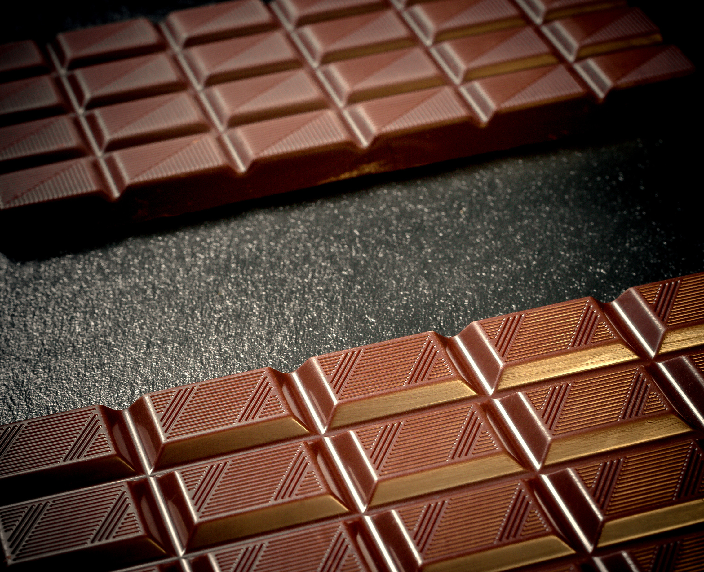 Two black chocolate bars on black slate plate, top view