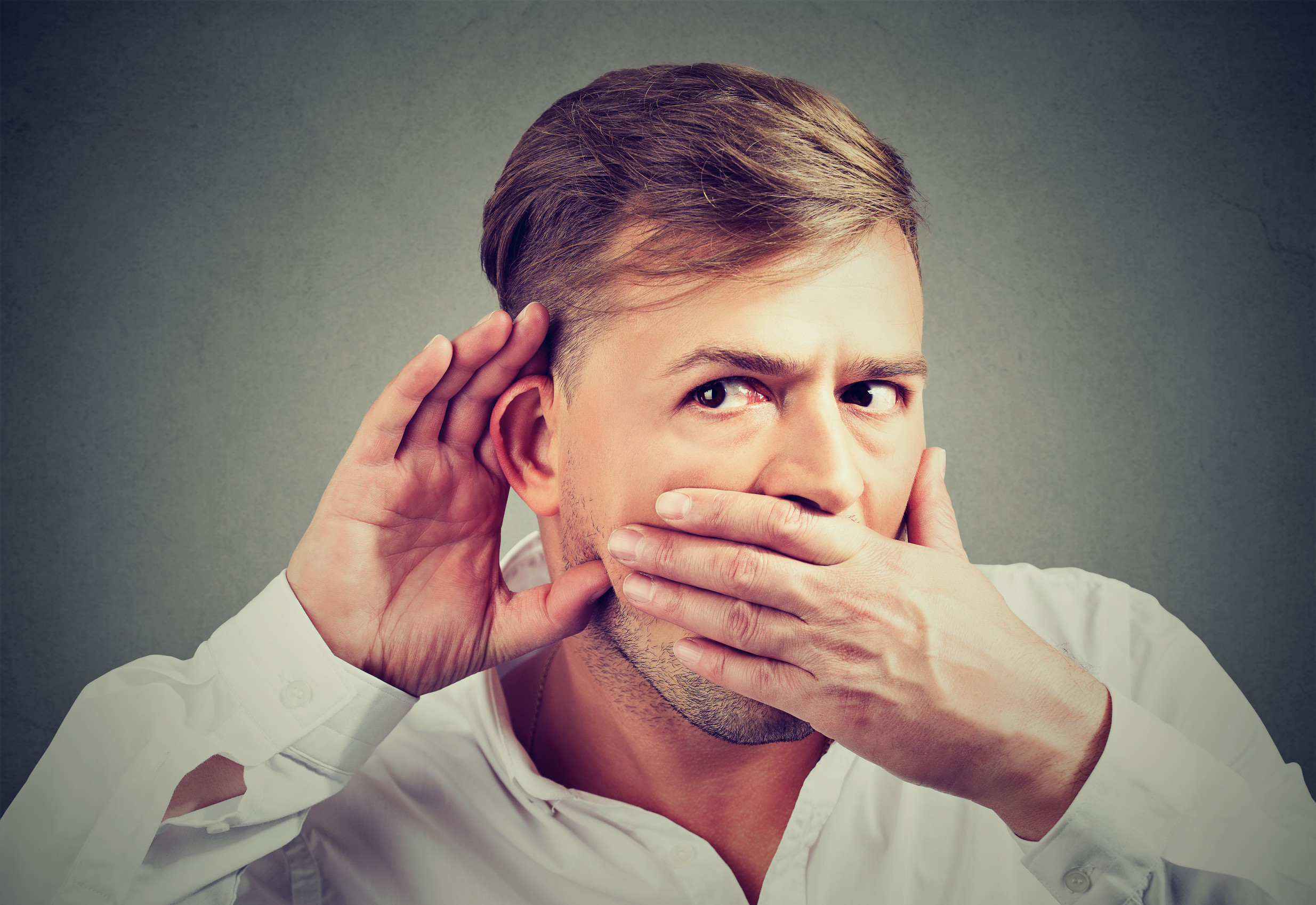 Young curious man holding hand to ear with mouth covered concentrated on eavesdropping a gossip.