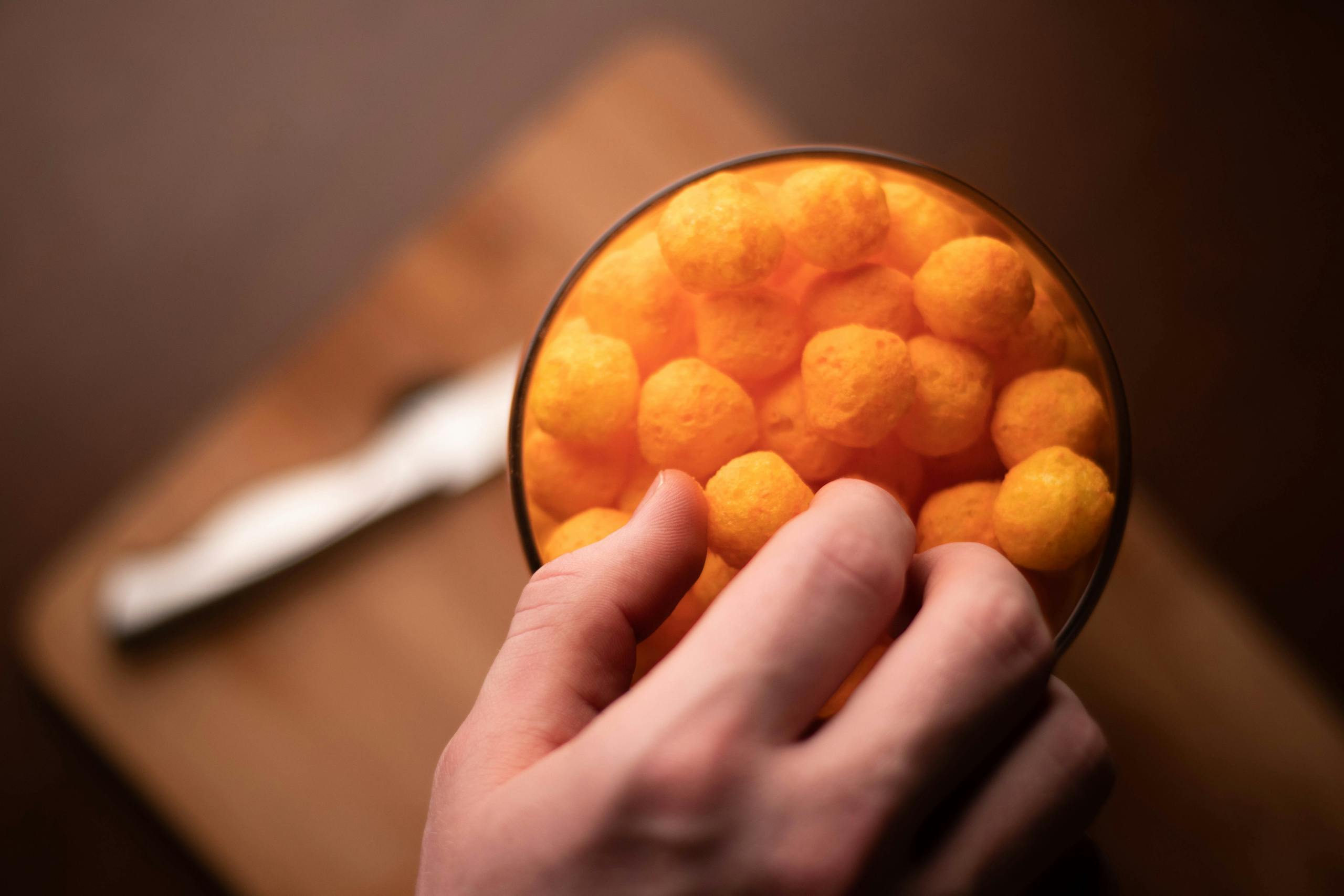 A hand reaching into a bowl of cheese puffs on a cutting board. High angle view.