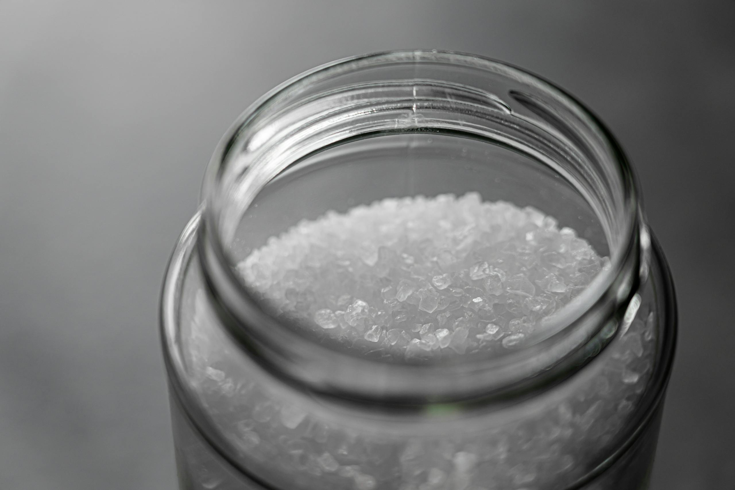 Close-up image of rock salt crystals inside an open glass jar, showcasing texture and clarity.