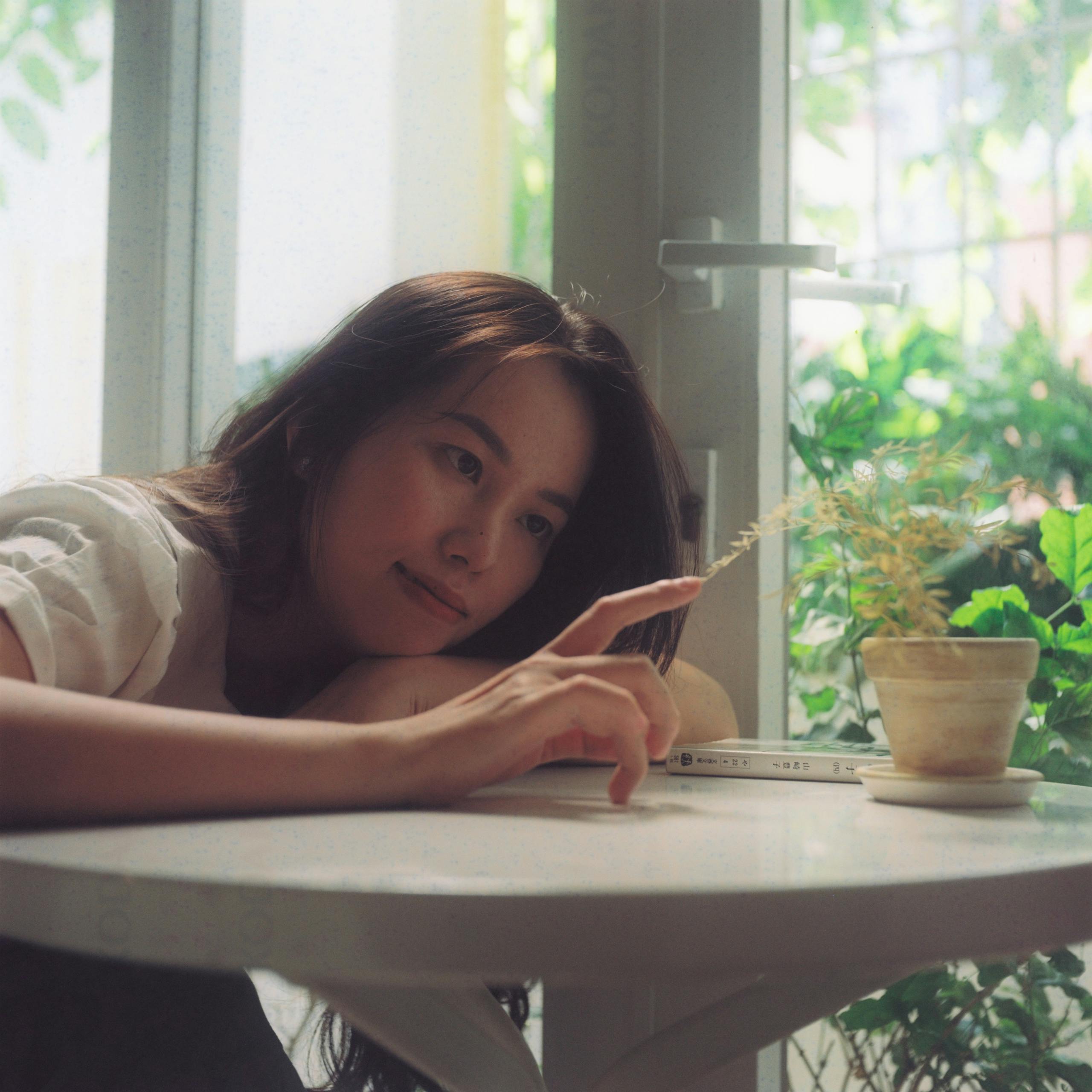 A woman relaxes at a table with a potted plant, enjoying leisure time indoors.