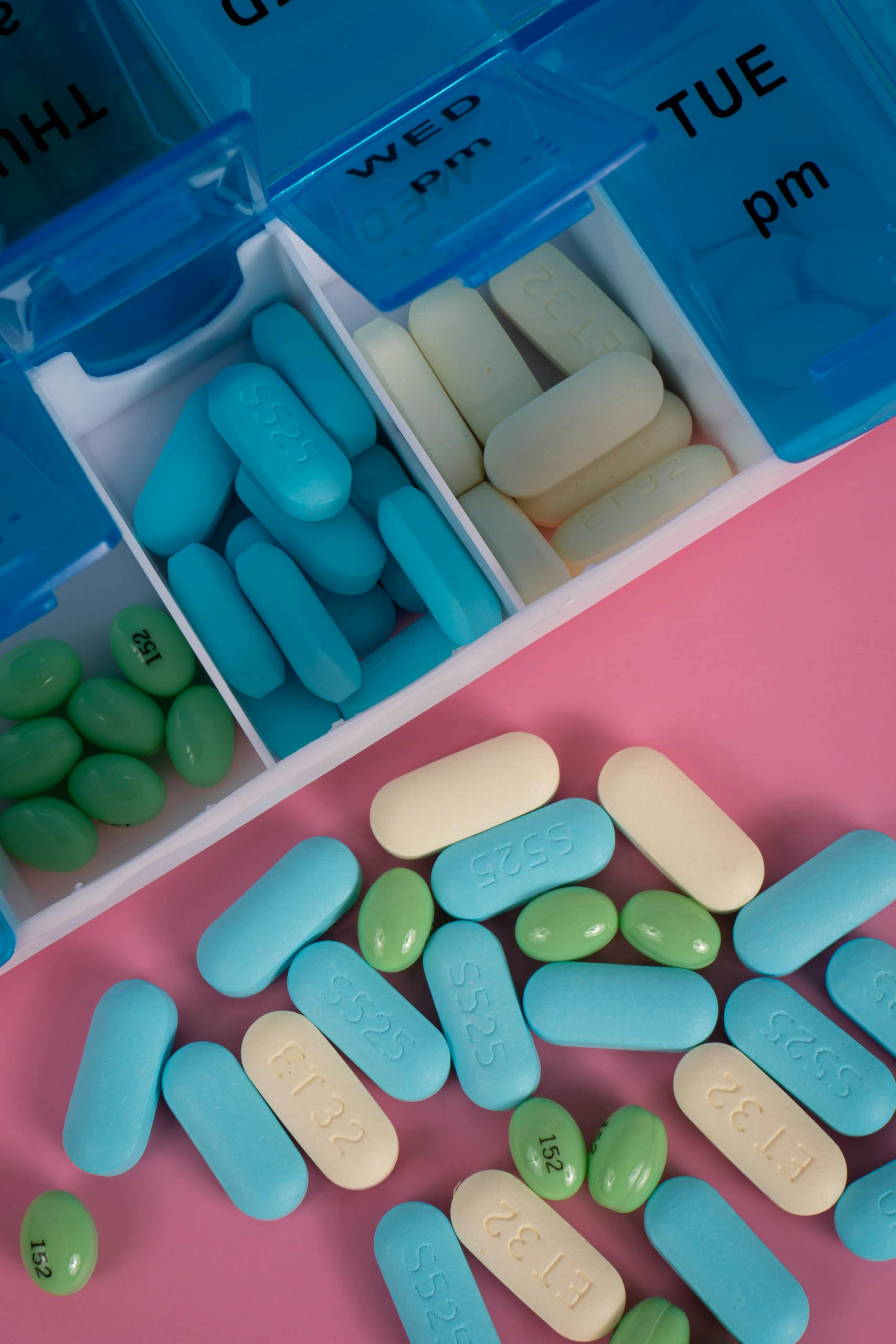 Colorful pills in a weekly organizer on a vibrant pink background.