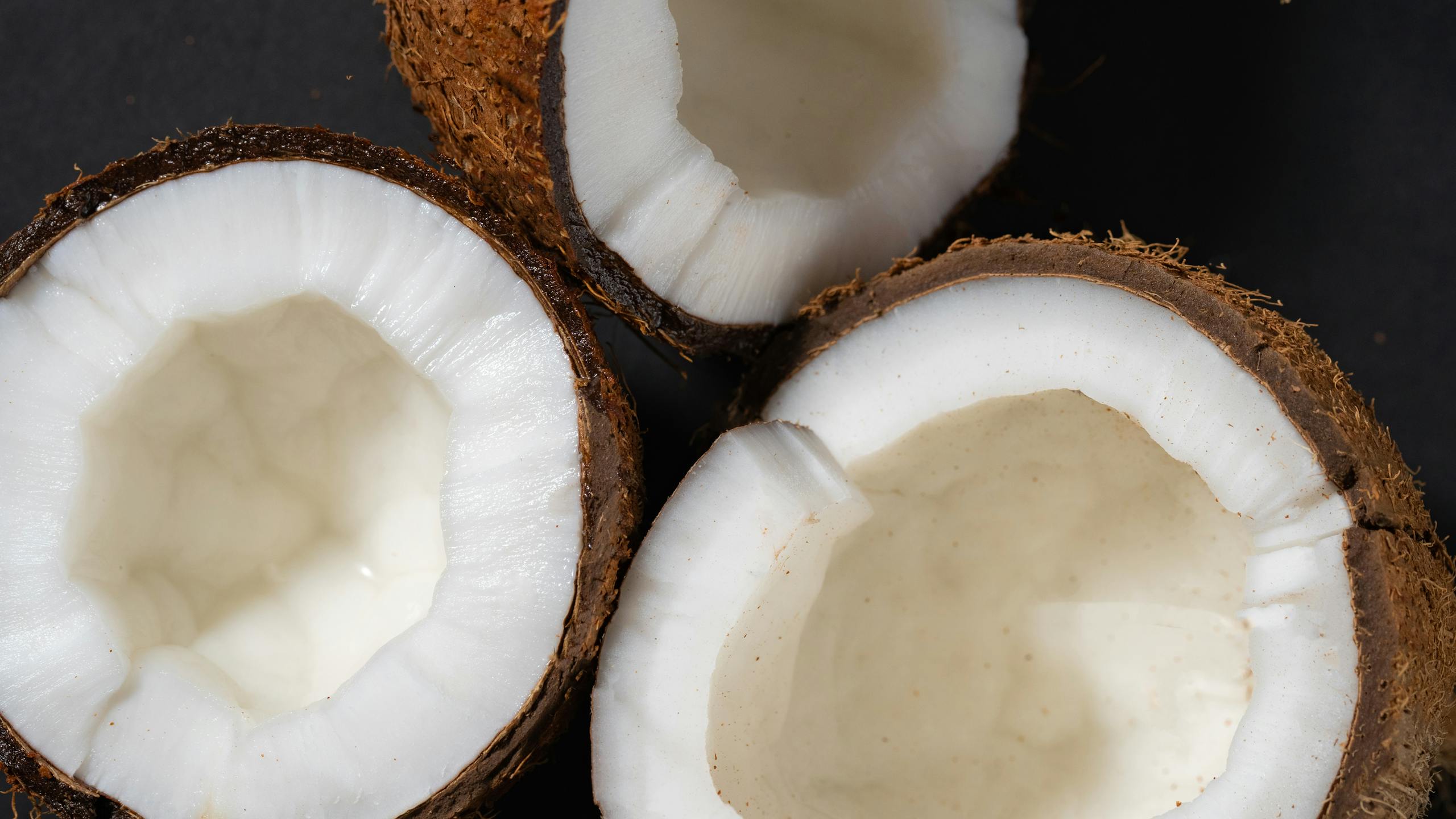 High-resolution image of three coconut halves revealing the fresh white kernel inside the brown shell.