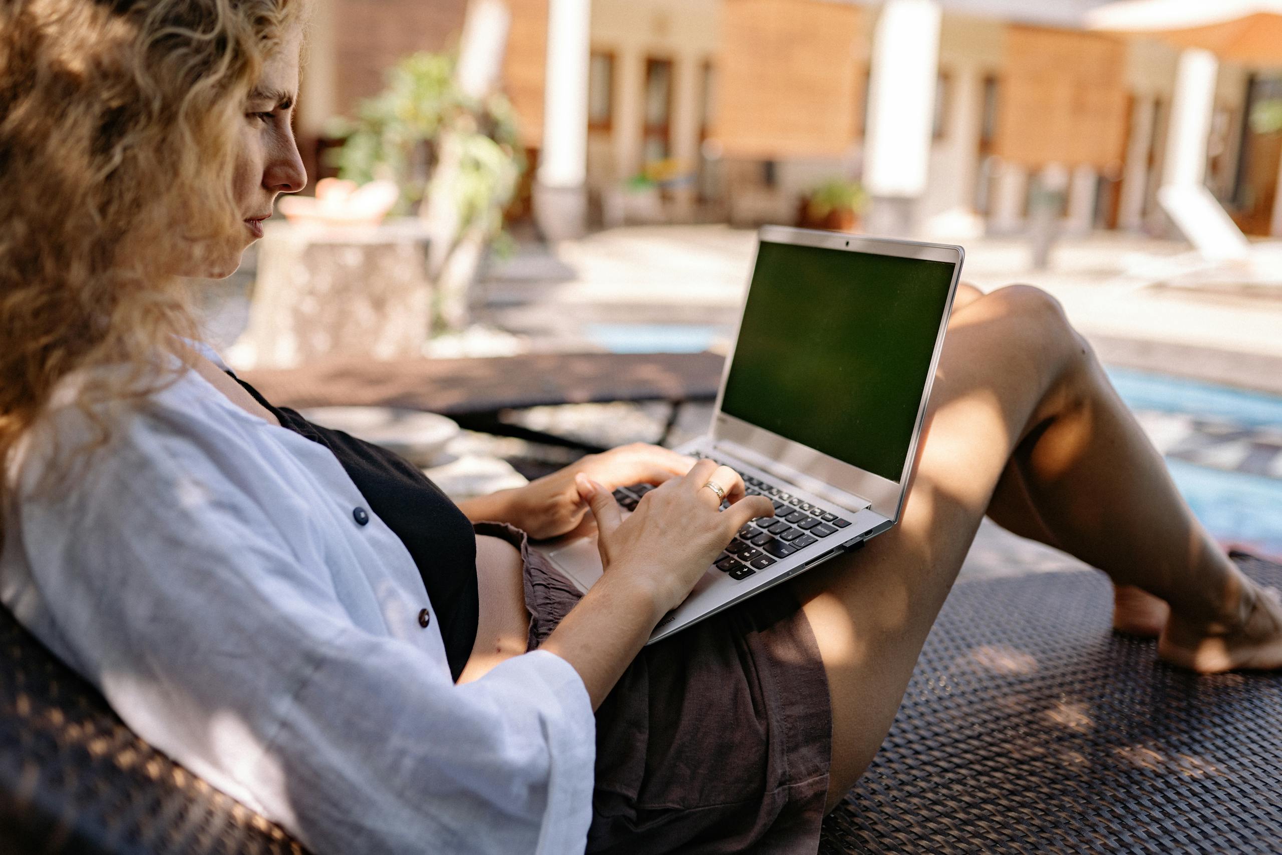 Relaxing professional woman working on a laptop outdoors by the poolside.