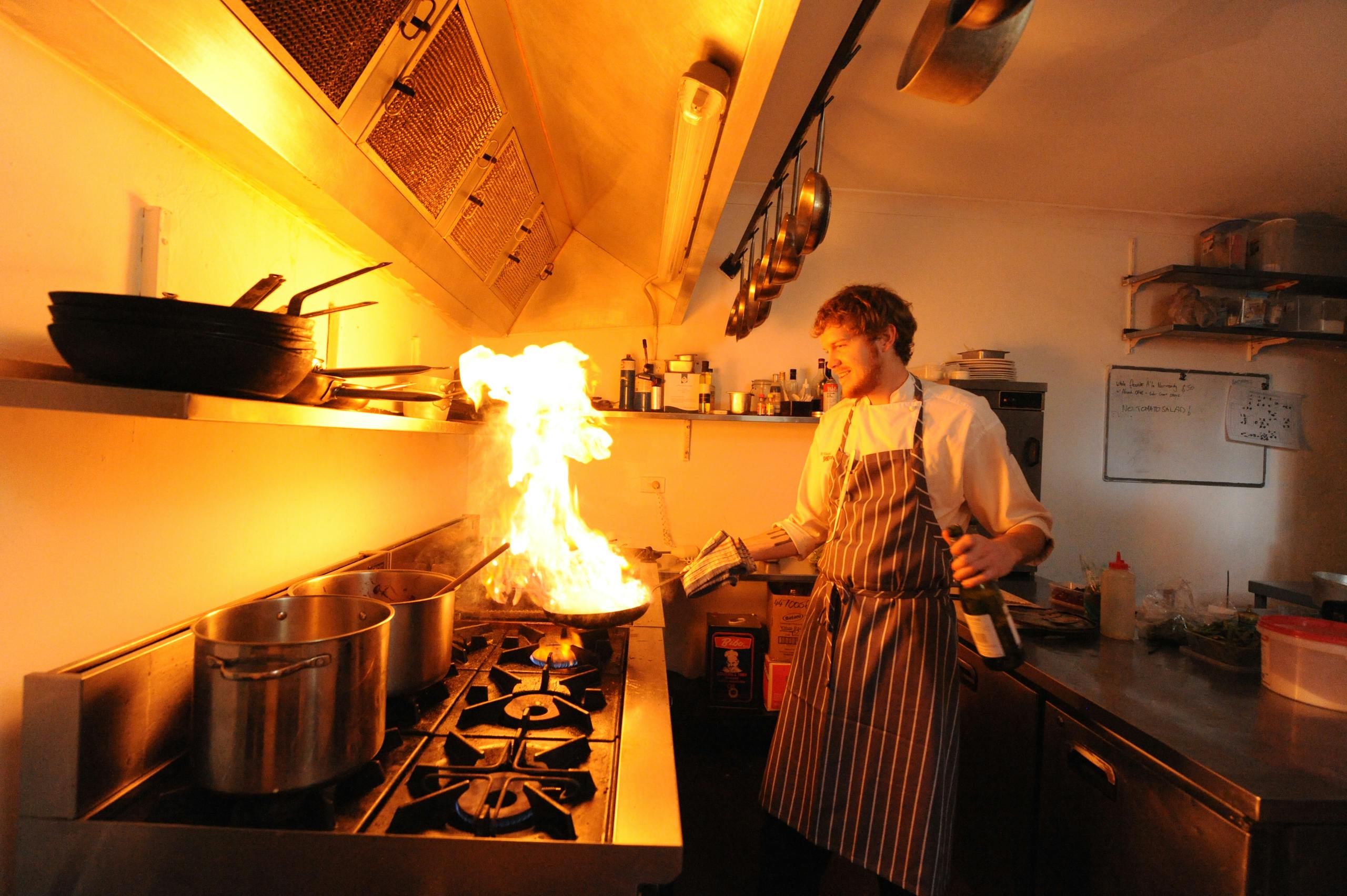 A chef expertly flambés a dish in a busy restaurant kitchen, creating a dramatic flame.