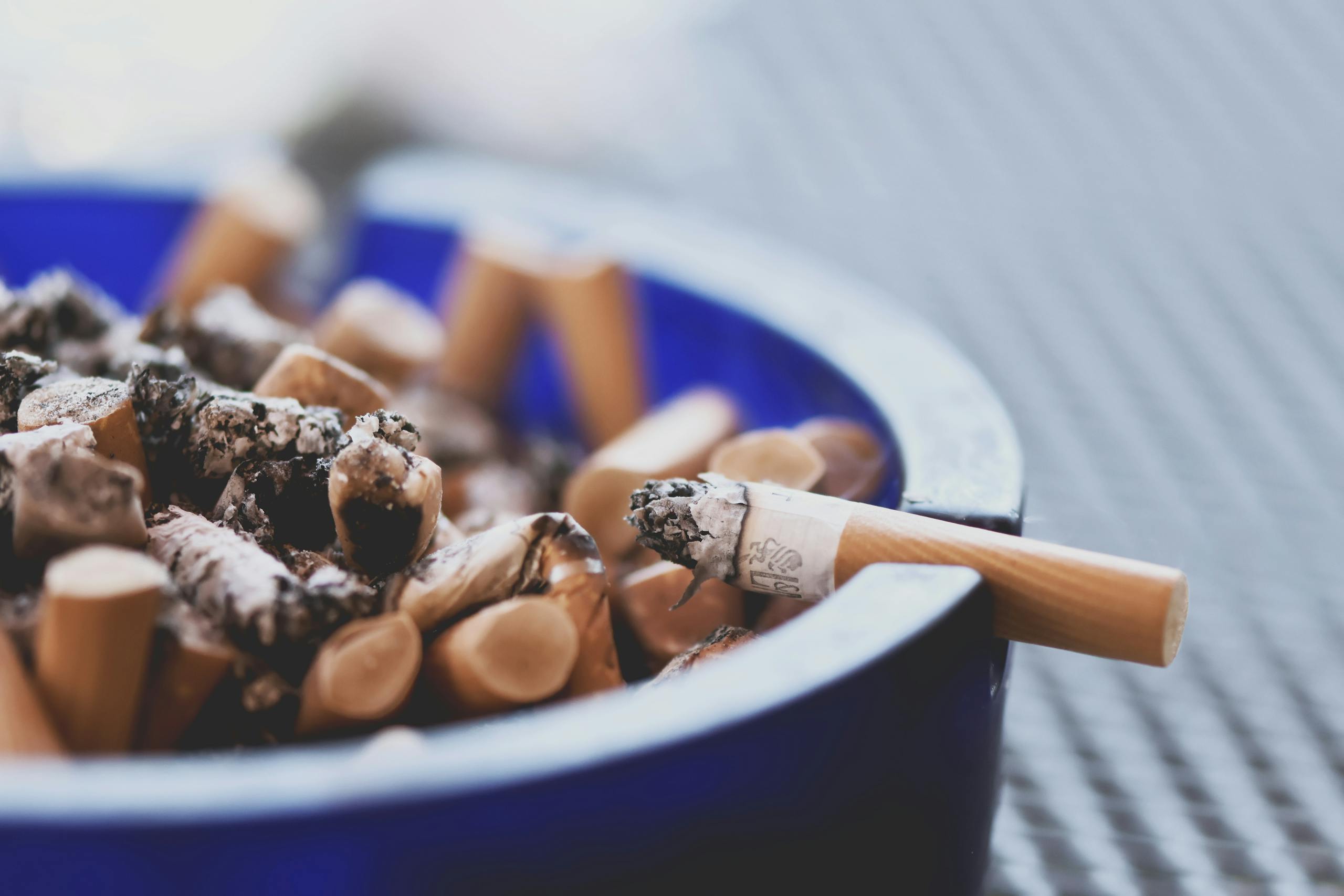 A close-up of cigarette butts in a blue ashtray, highlighting tobacco consumption.