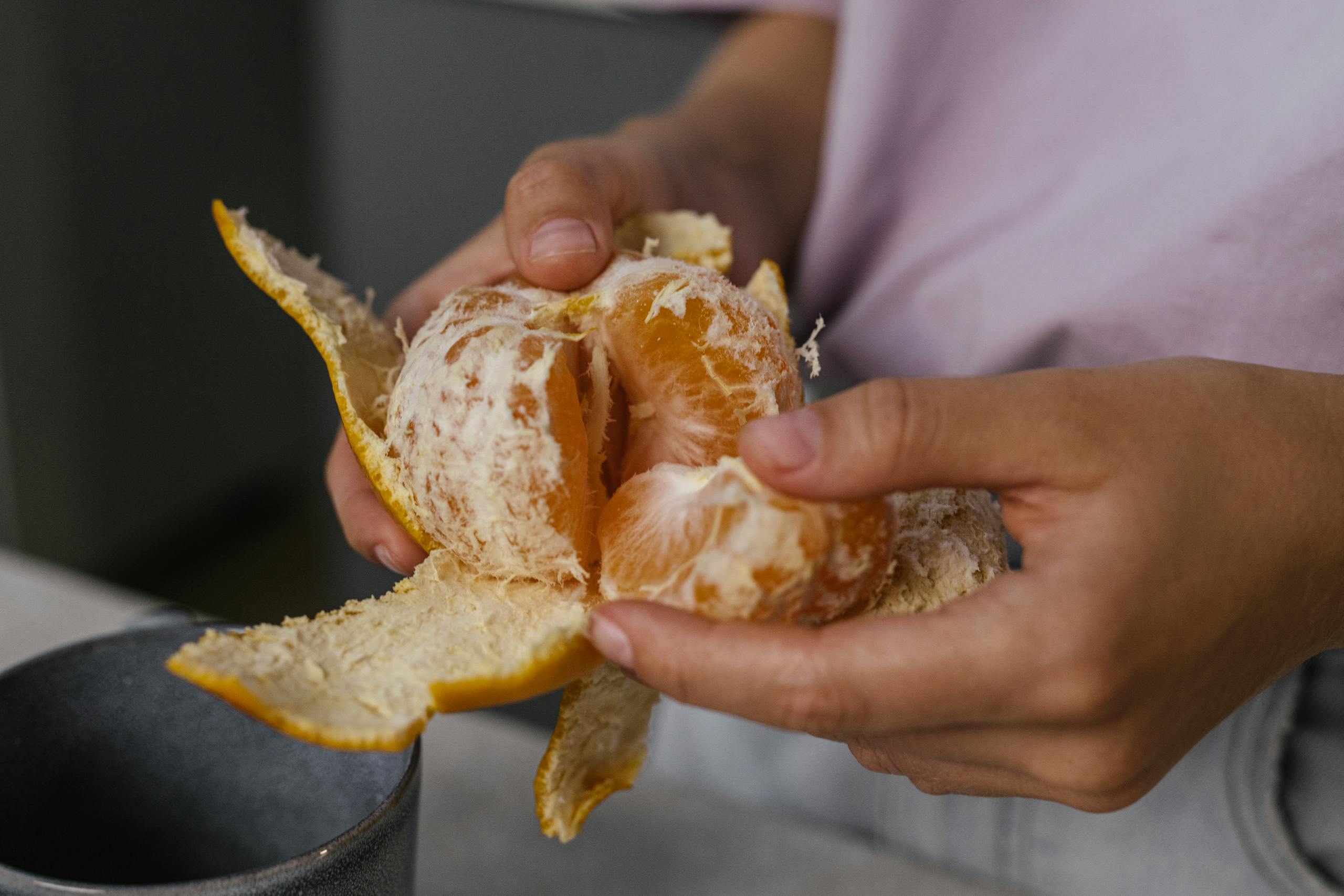 A close-up shot of hands peeling a fresh orange, showcasing the juicy texture of the fruit.