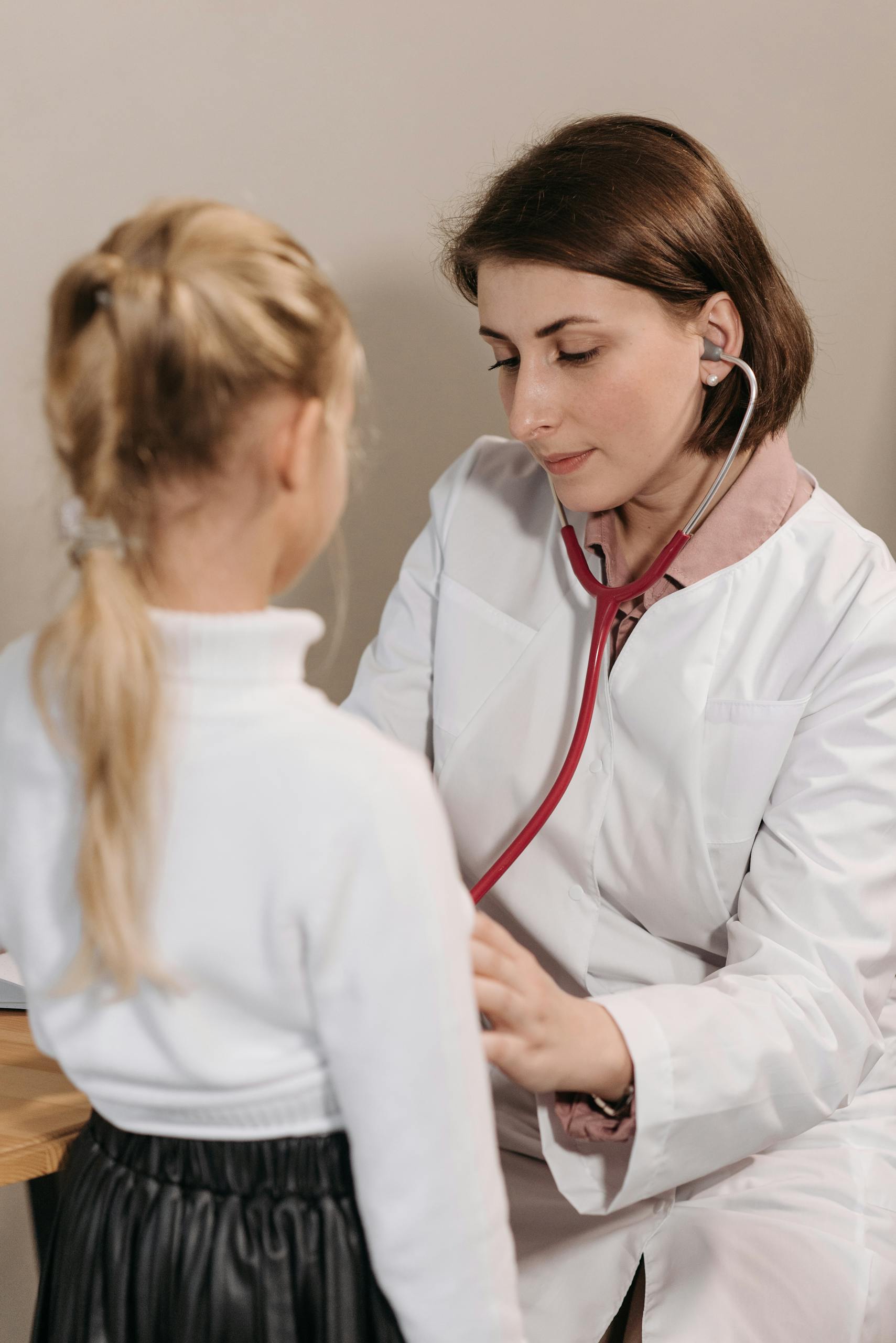 A female doctor examining a child with a stethoscope during a pediatric check-up in a clinic.