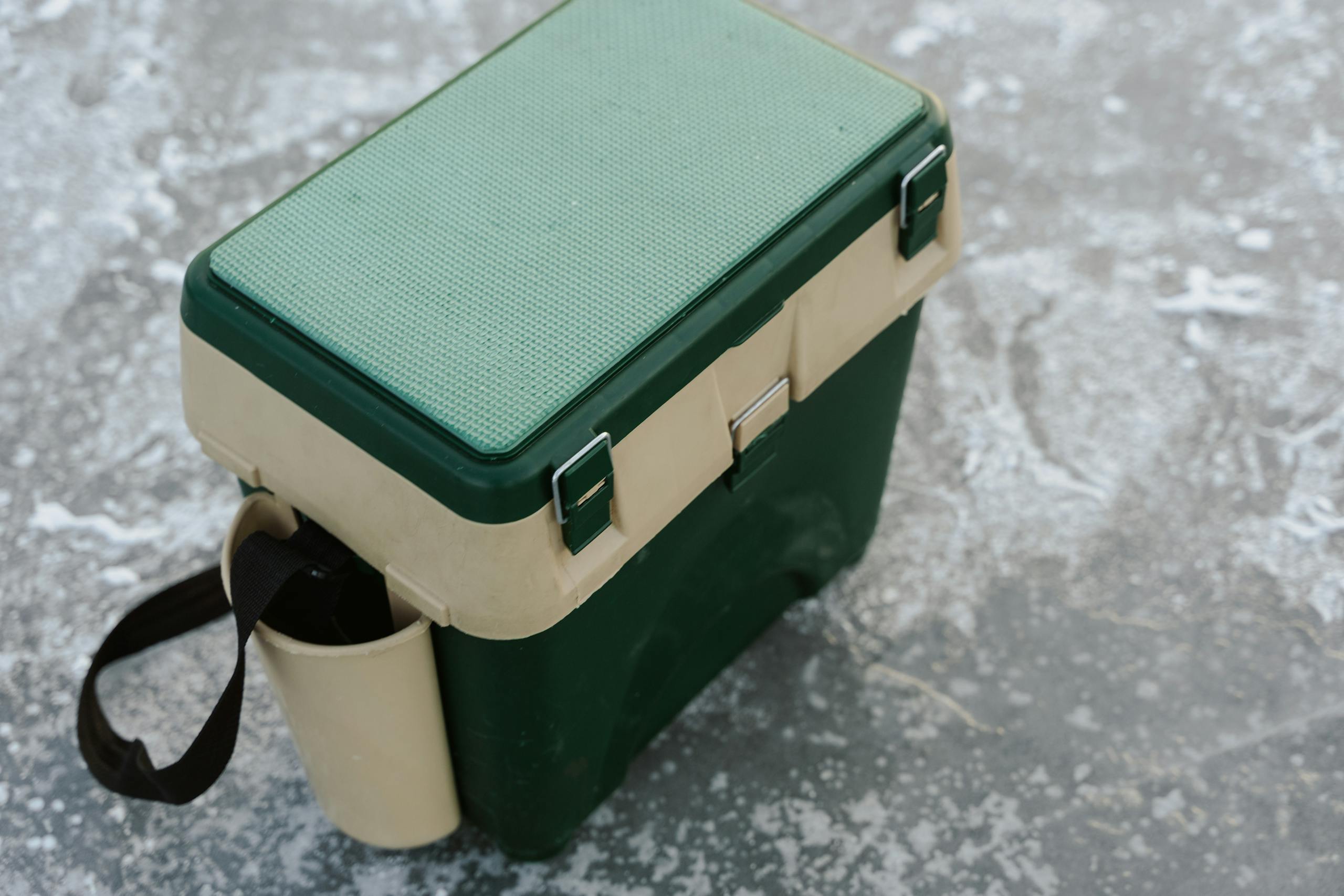 A green and beige cooler sits on a frozen ice surface, ideal for outdoor adventures.