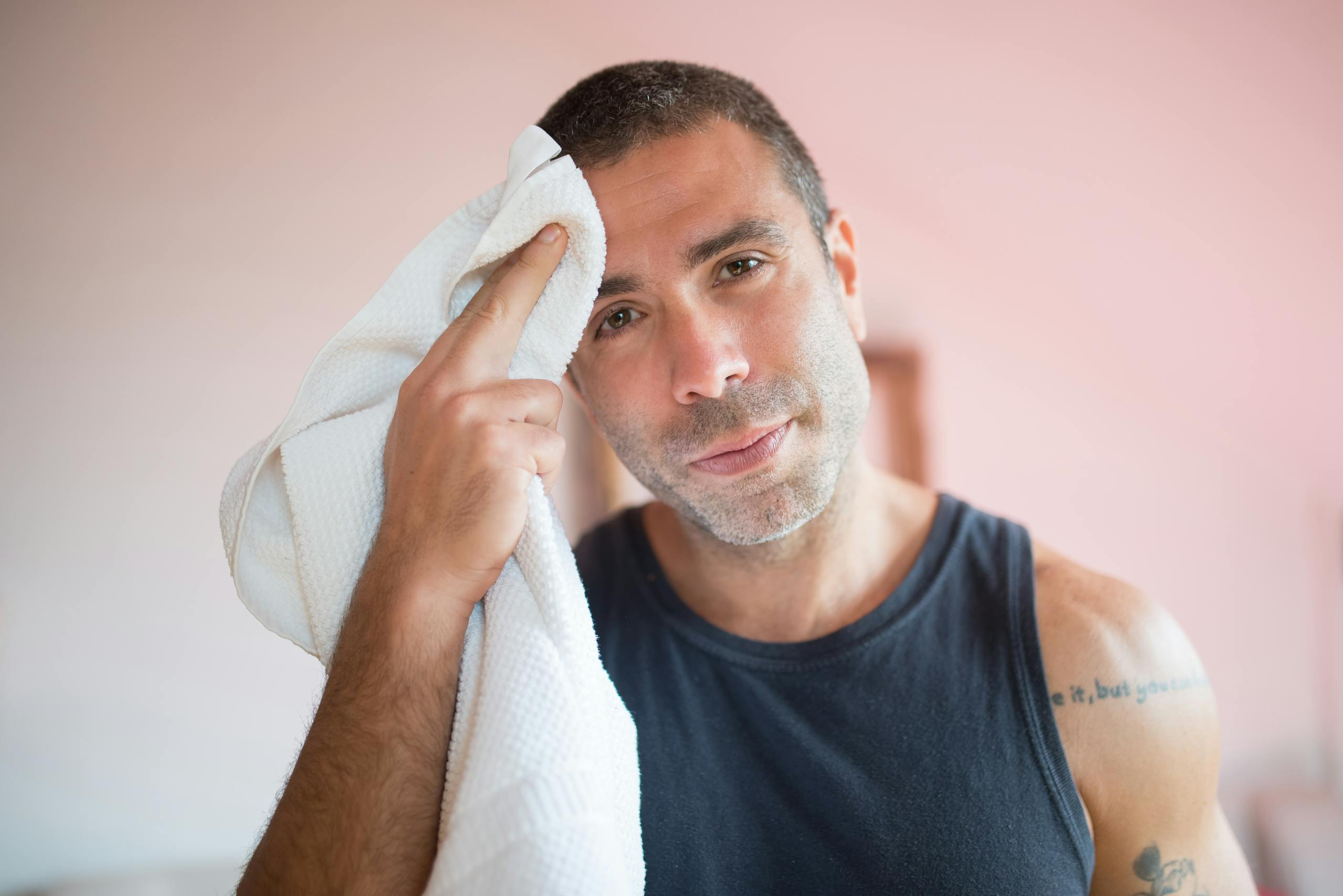 A man wipes sweat with a towel indoors, showcasing post-exercise relaxation.
