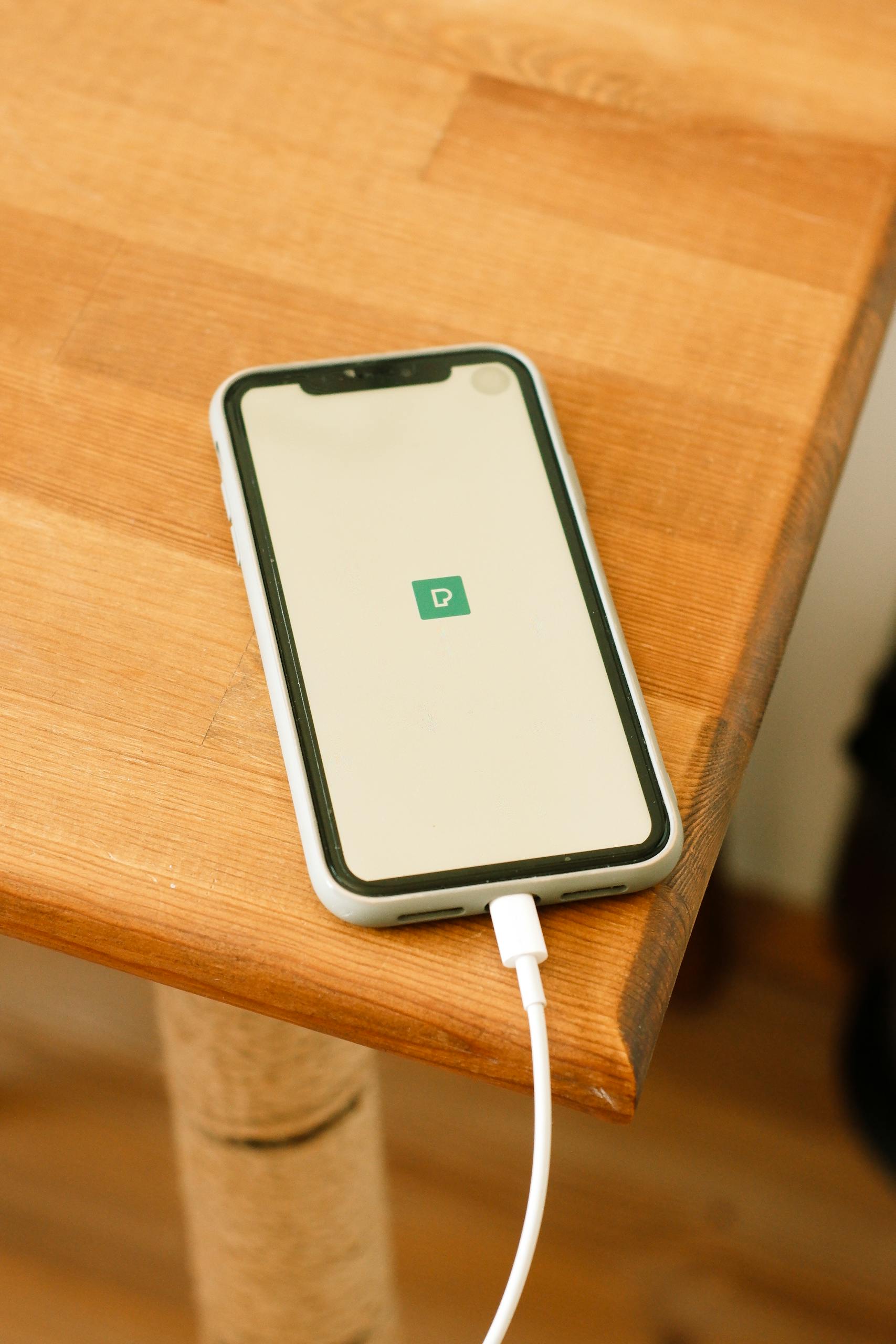 A smartphone connects to a charger on a wooden table, highlighting modern technology.