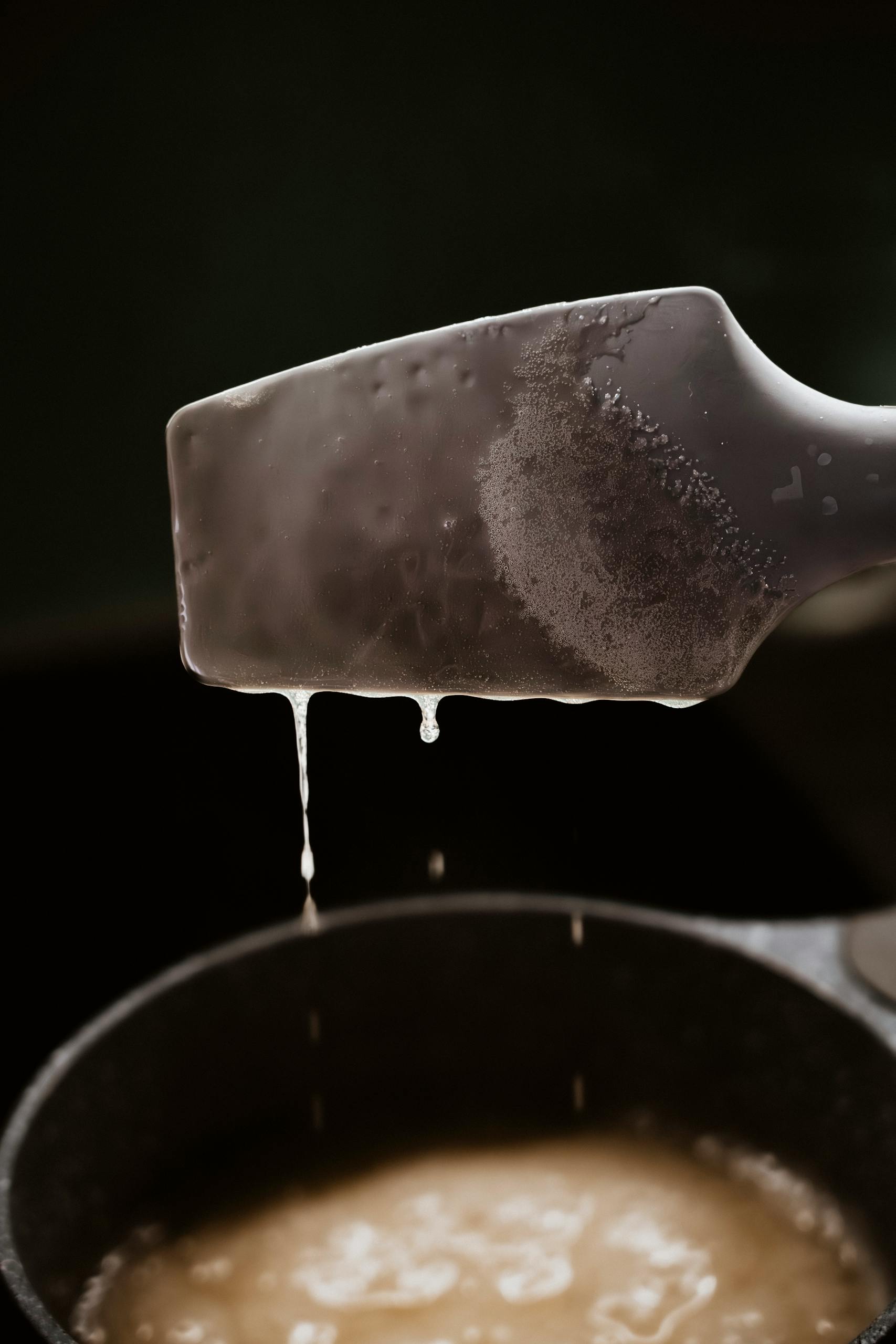A spatula dripping grease over a pan, showcasing culinary cooking concept.
