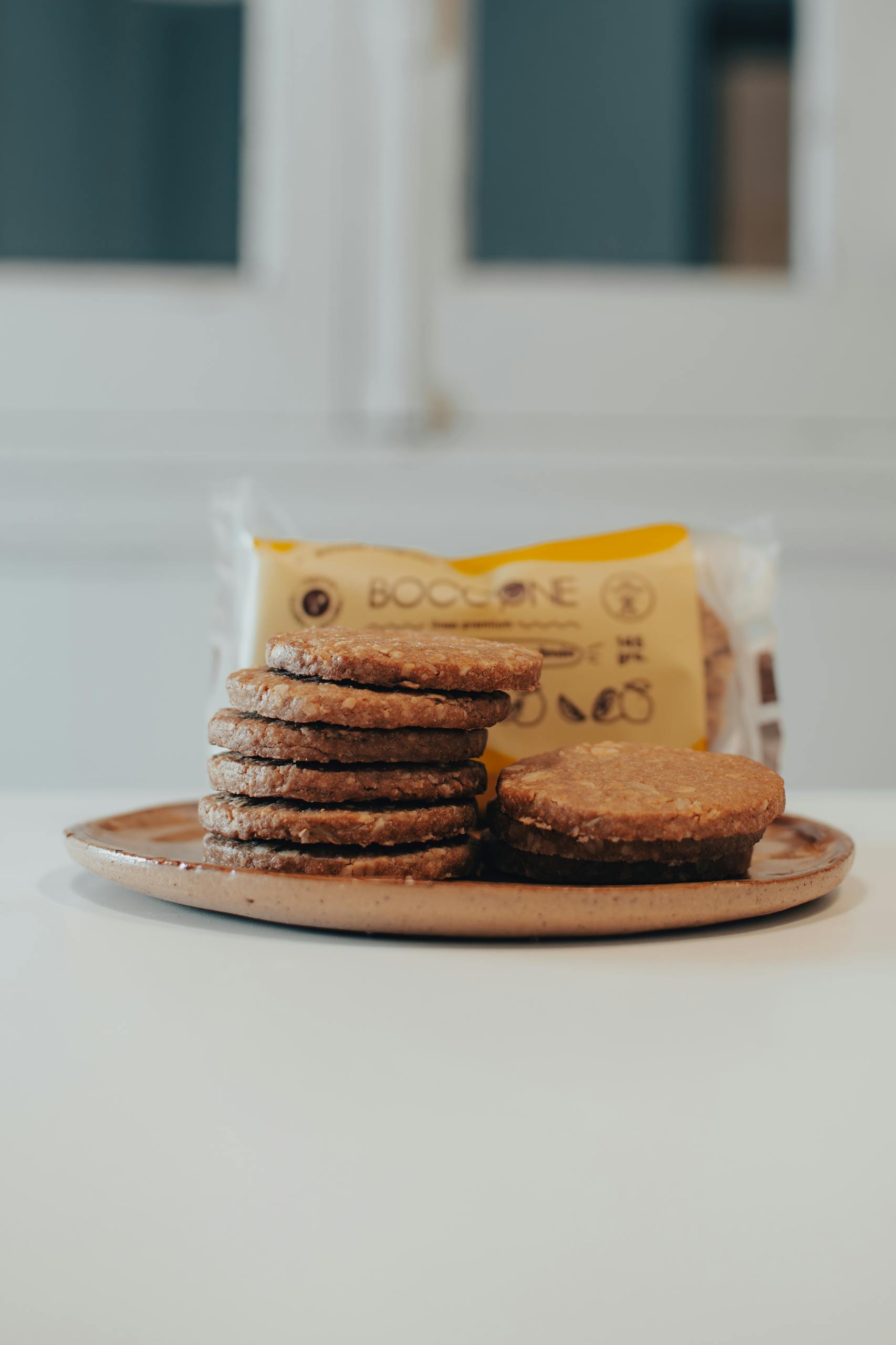 A stack of gourmet cookies on a rustic plate with a blurred package in the background.