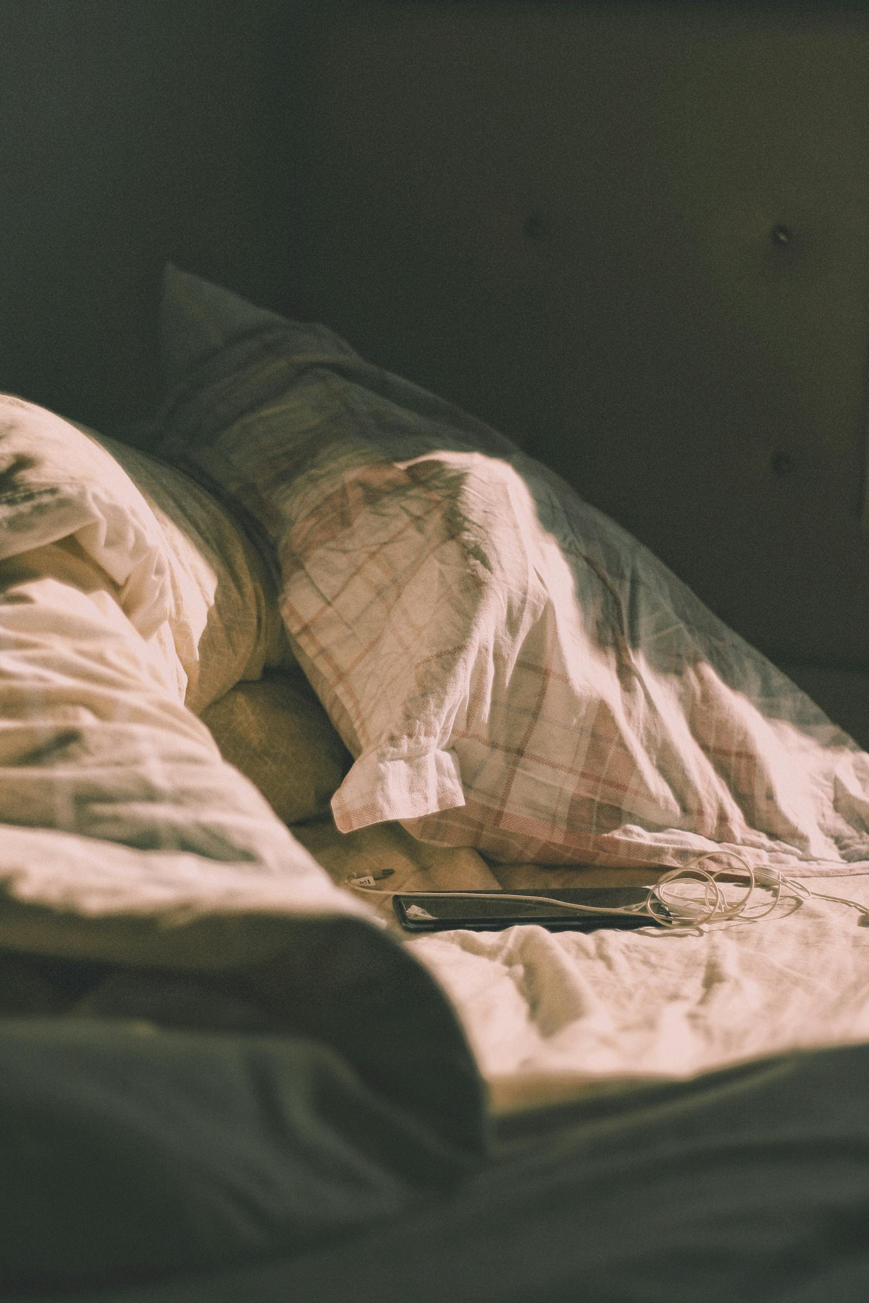 Sunlit bedroom with cozy bedding and smartphone on the sheets, creating a warm, relaxed atmosphere.