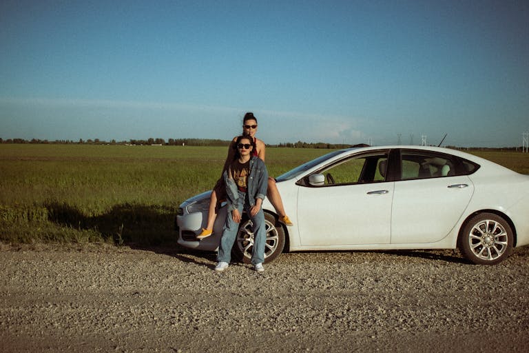 Two adults enjoying a scenic road trip stop by a white car in a field.