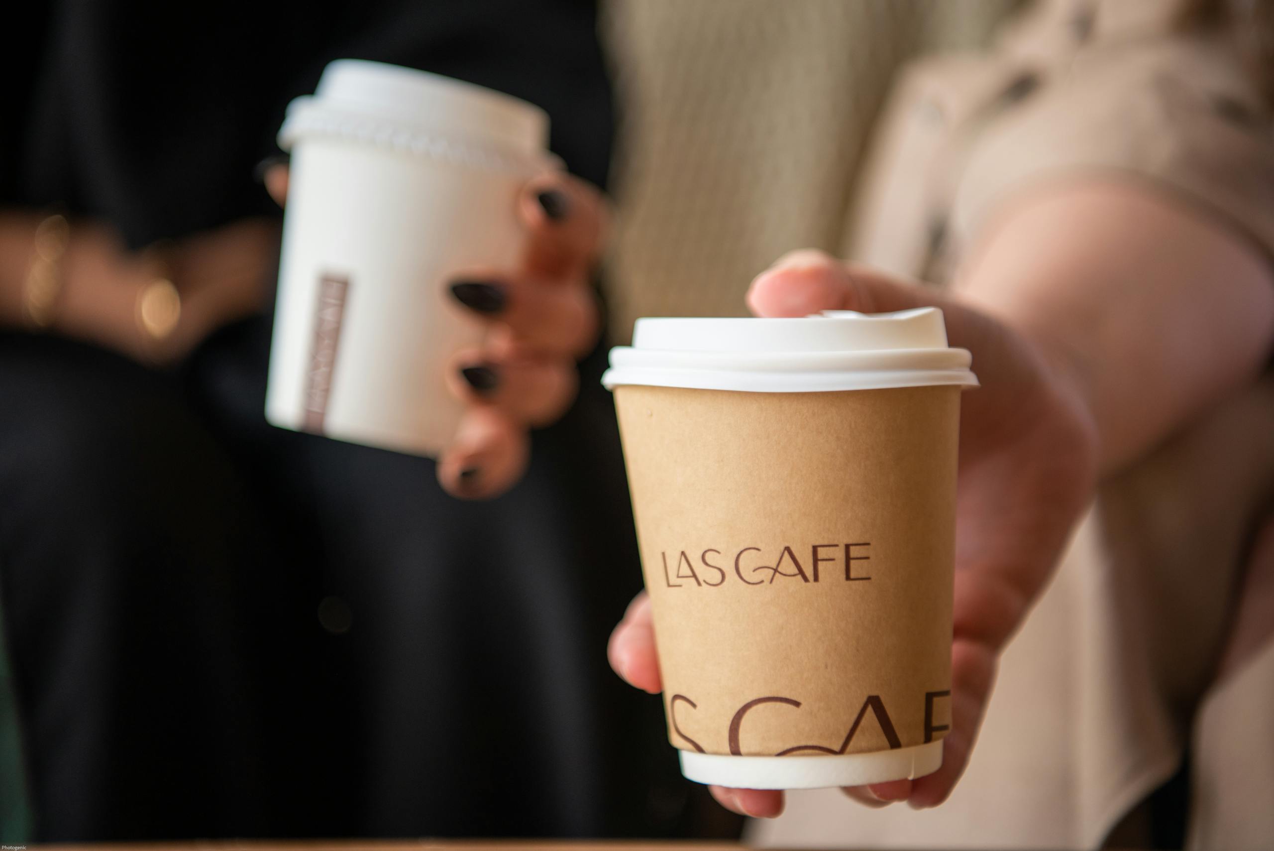 Two people holding coffee cups labeled Las Cafe, close-up and stylish.
