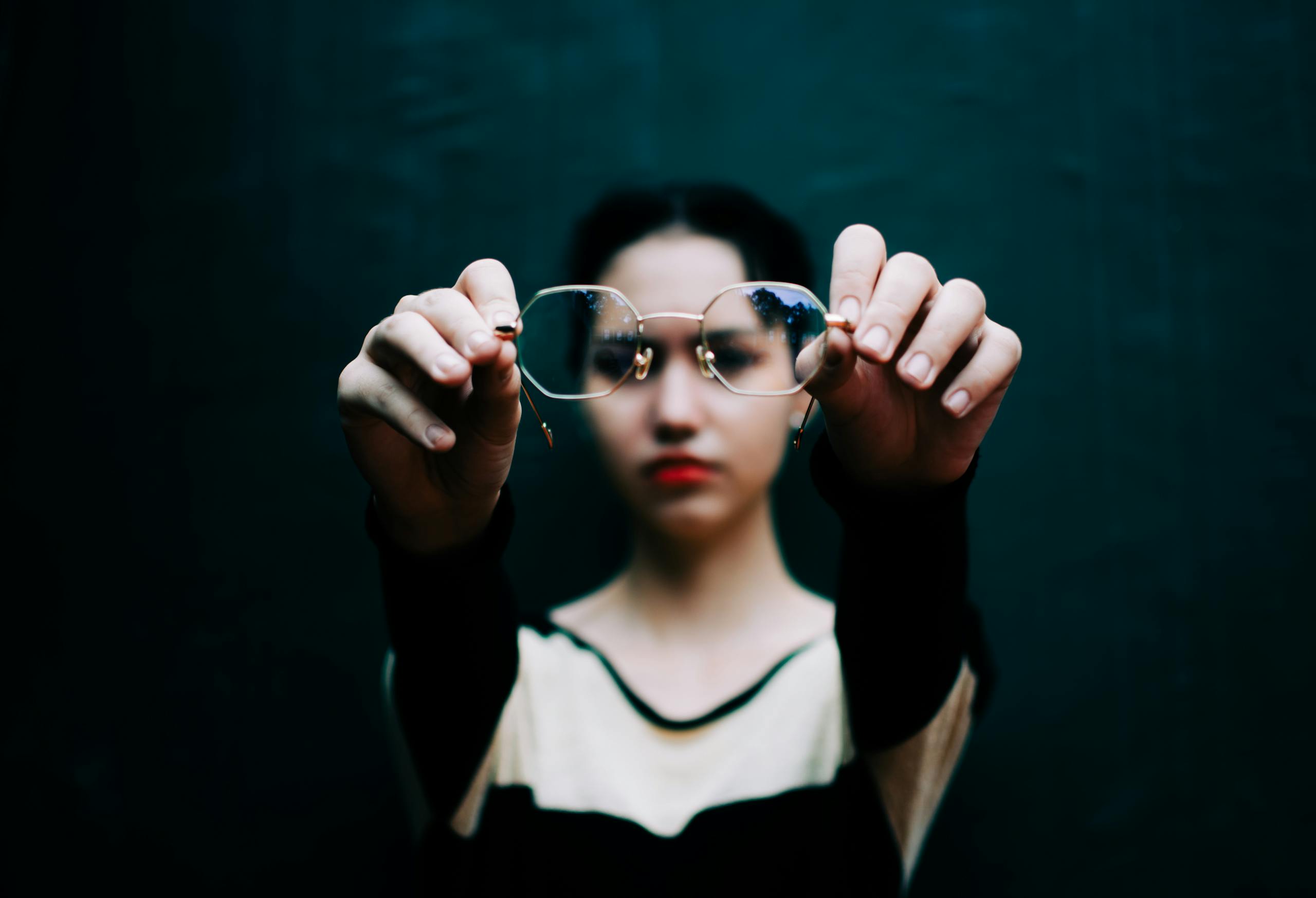 Selective focus of eyeglasses in hands of lady with red lips against black background
