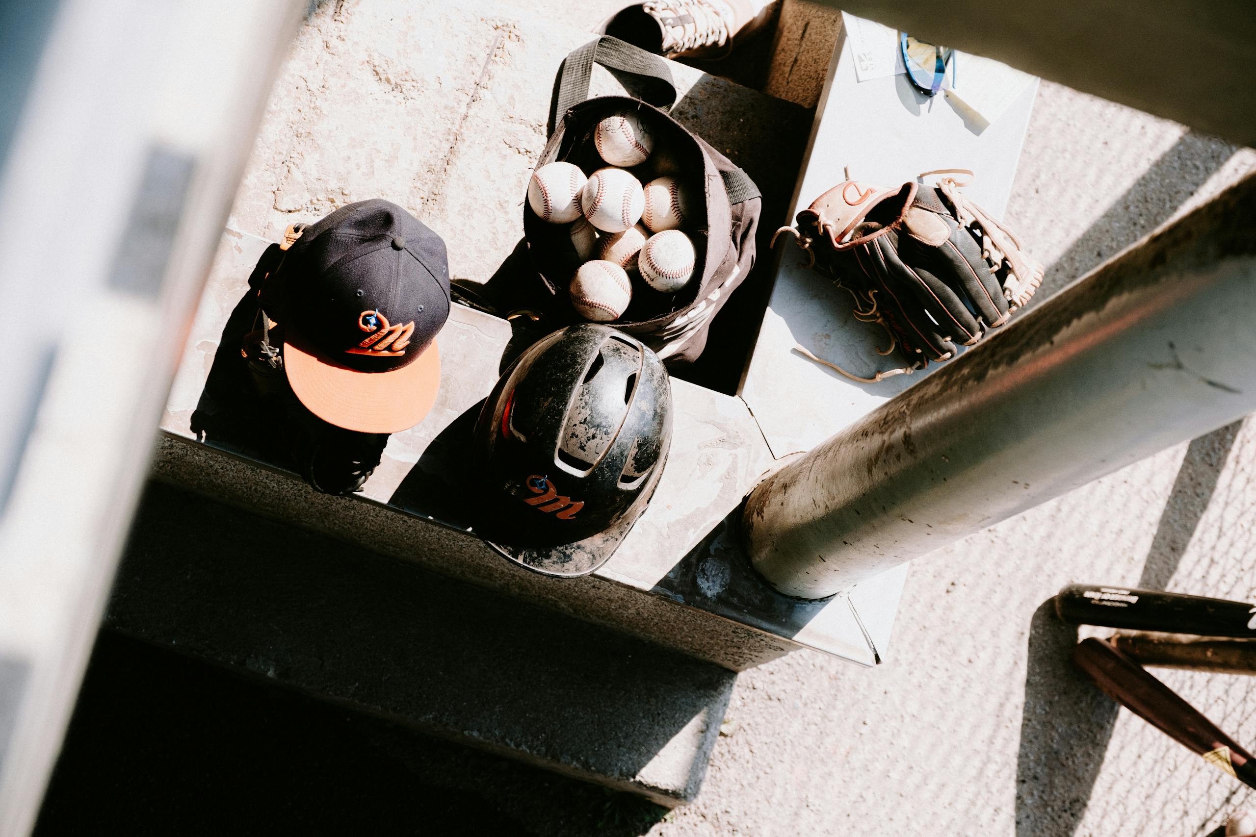 Top view of baseball gear including helmets, cap, gloves, and balls on the steps.