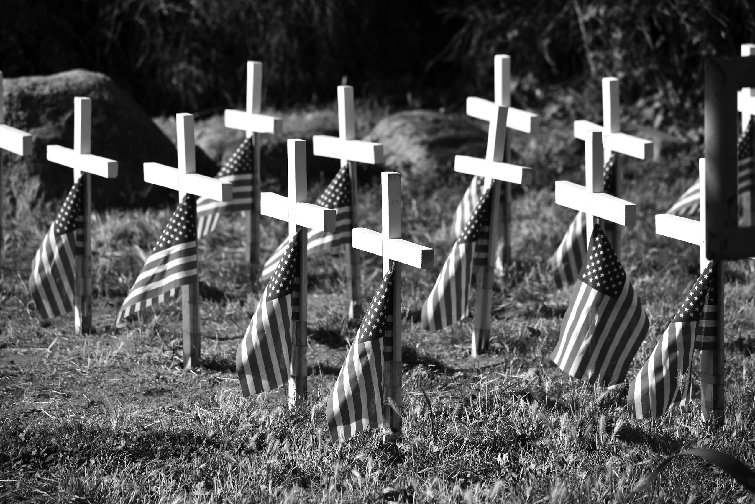 Black and white image of cemetery crosses adorned with American flags, symbolizing remembrance.