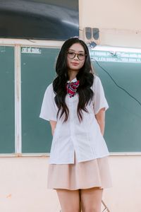 Young woman in school uniform standing before classroom chalkboard.