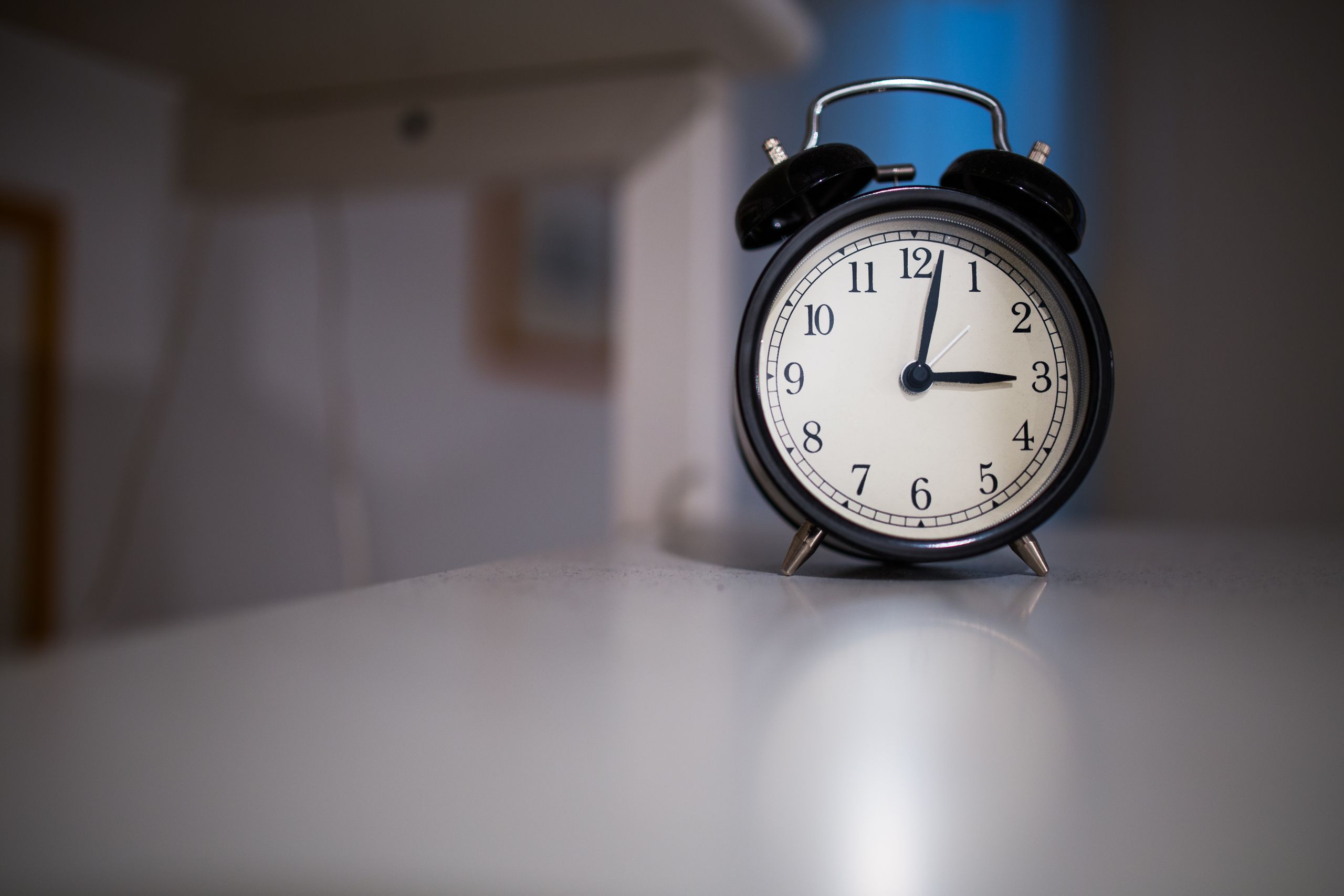 A classic black alarm clock with a white face showing 7:05, placed on a white surface.