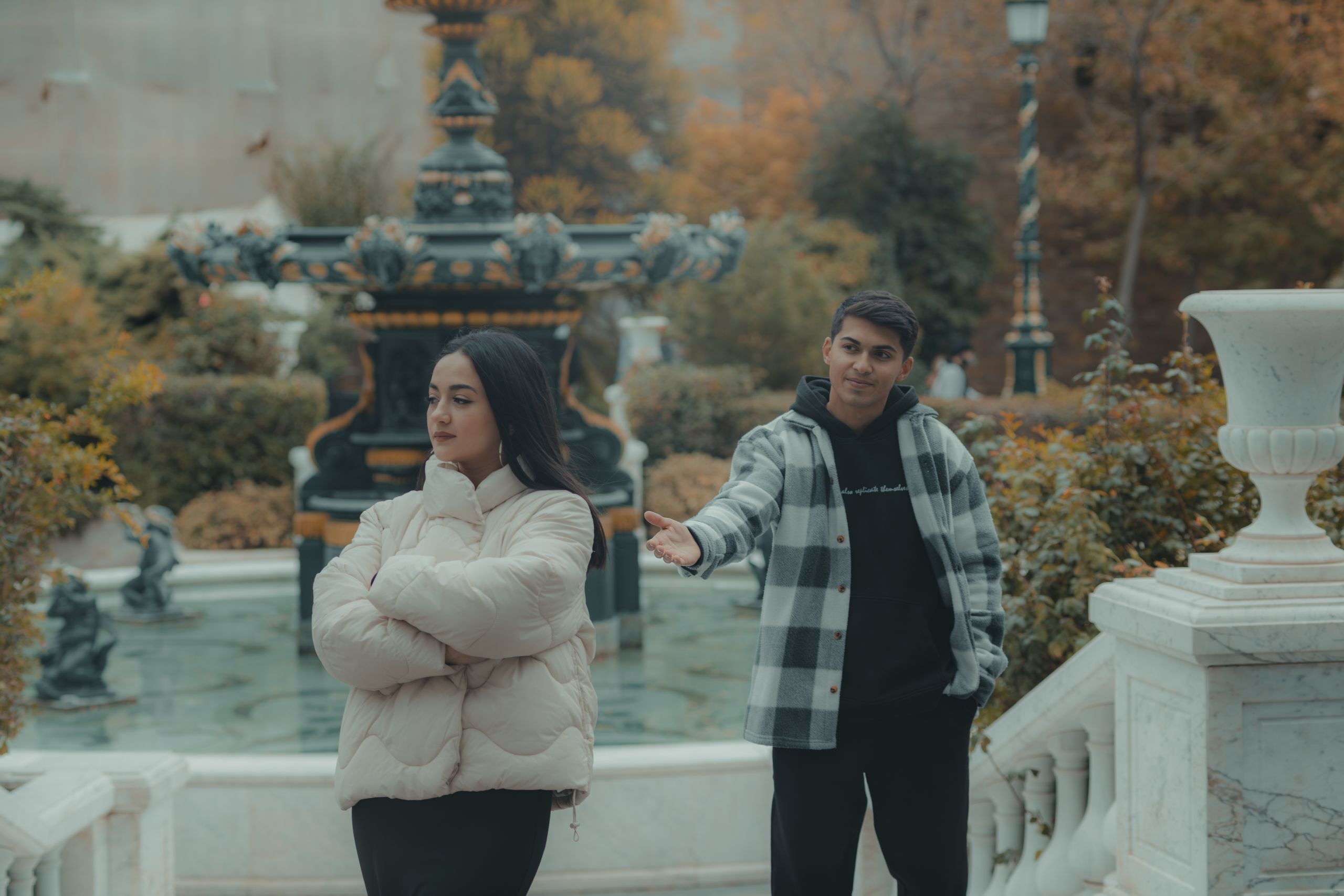 A couple shares a moment near an ornate fountain amidst autumn foliage in a park.