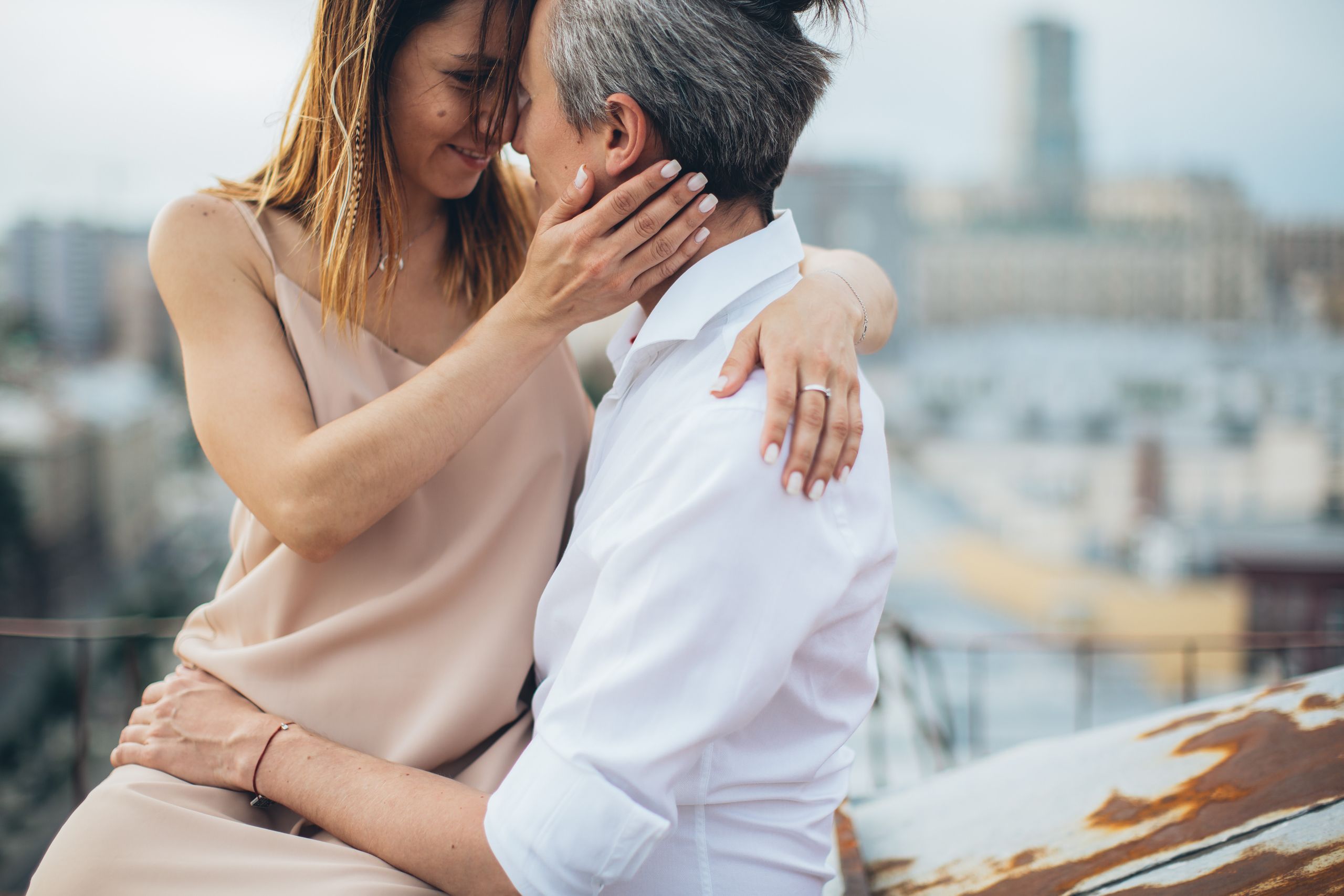 A loving couple shares an intimate moment on a rooftop with a blurred cityscape in the background.