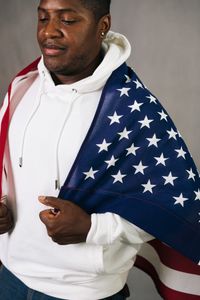 African American man in white hoodie wrapped in USA flag, showcasing patriotism and unity.