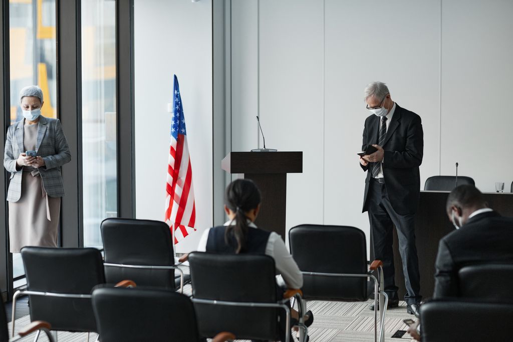 Business professionals in masks at a socially distanced meeting in an office with US flag.