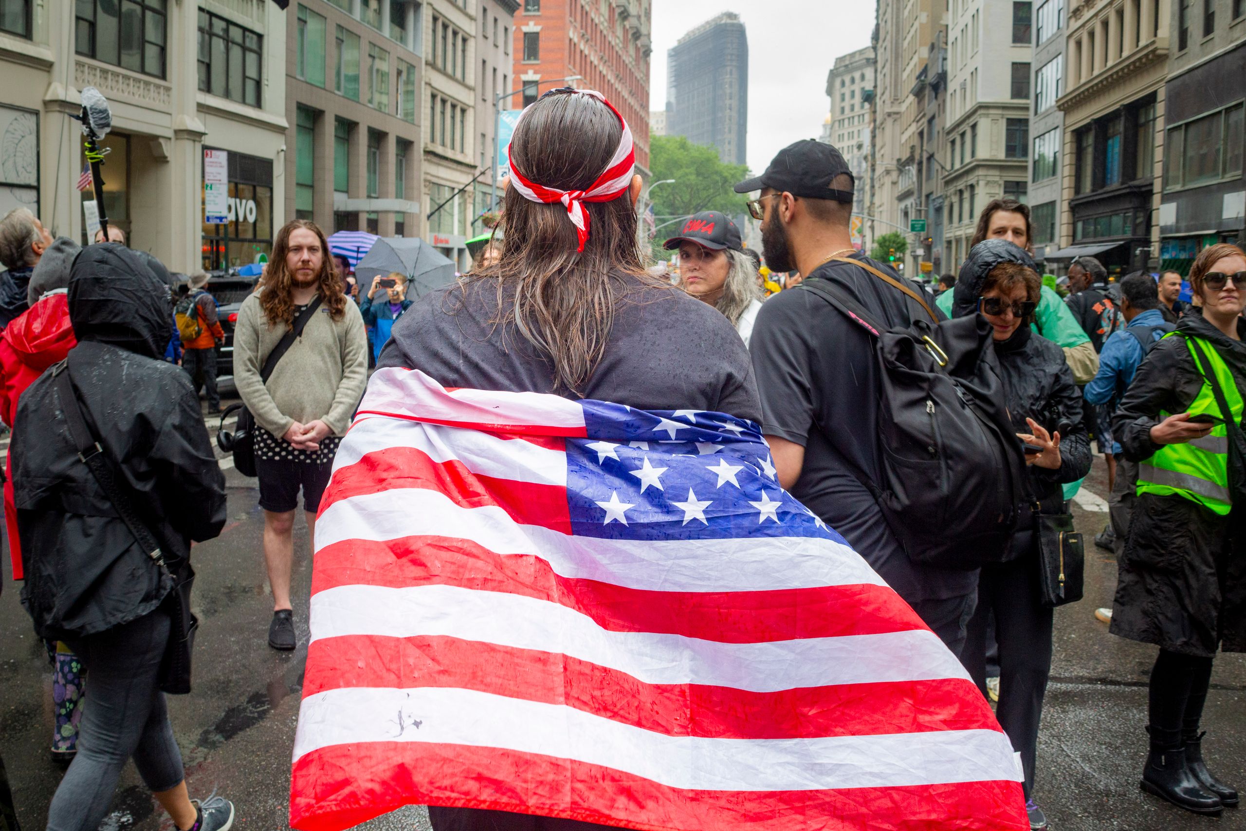People gather at a city street rally with American flag in rainy weather.