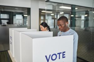 Two individuals casting votes in an indoor voting booth, emphasizing democracy.