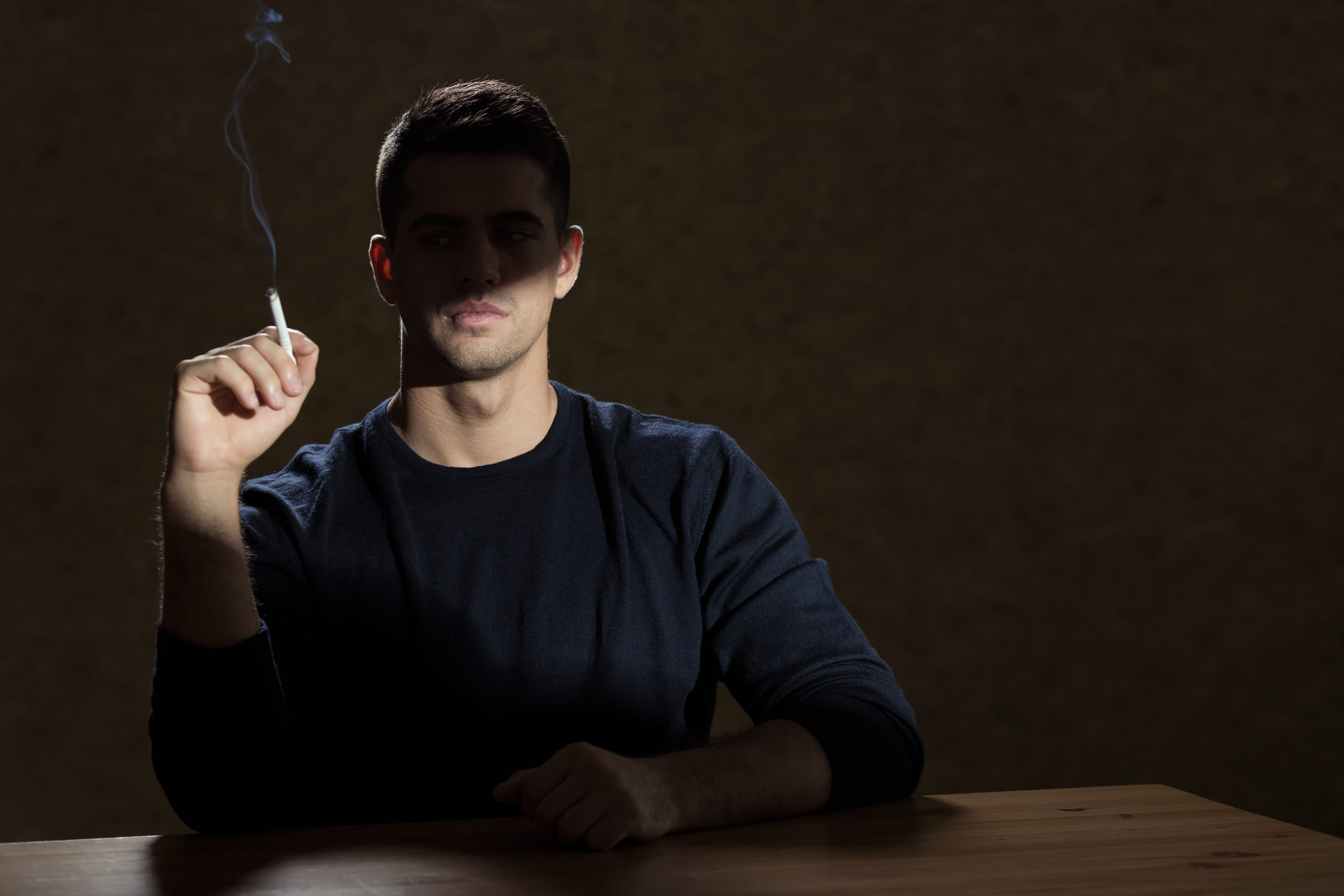 Young man sitting in dark interior, smoking cigarette