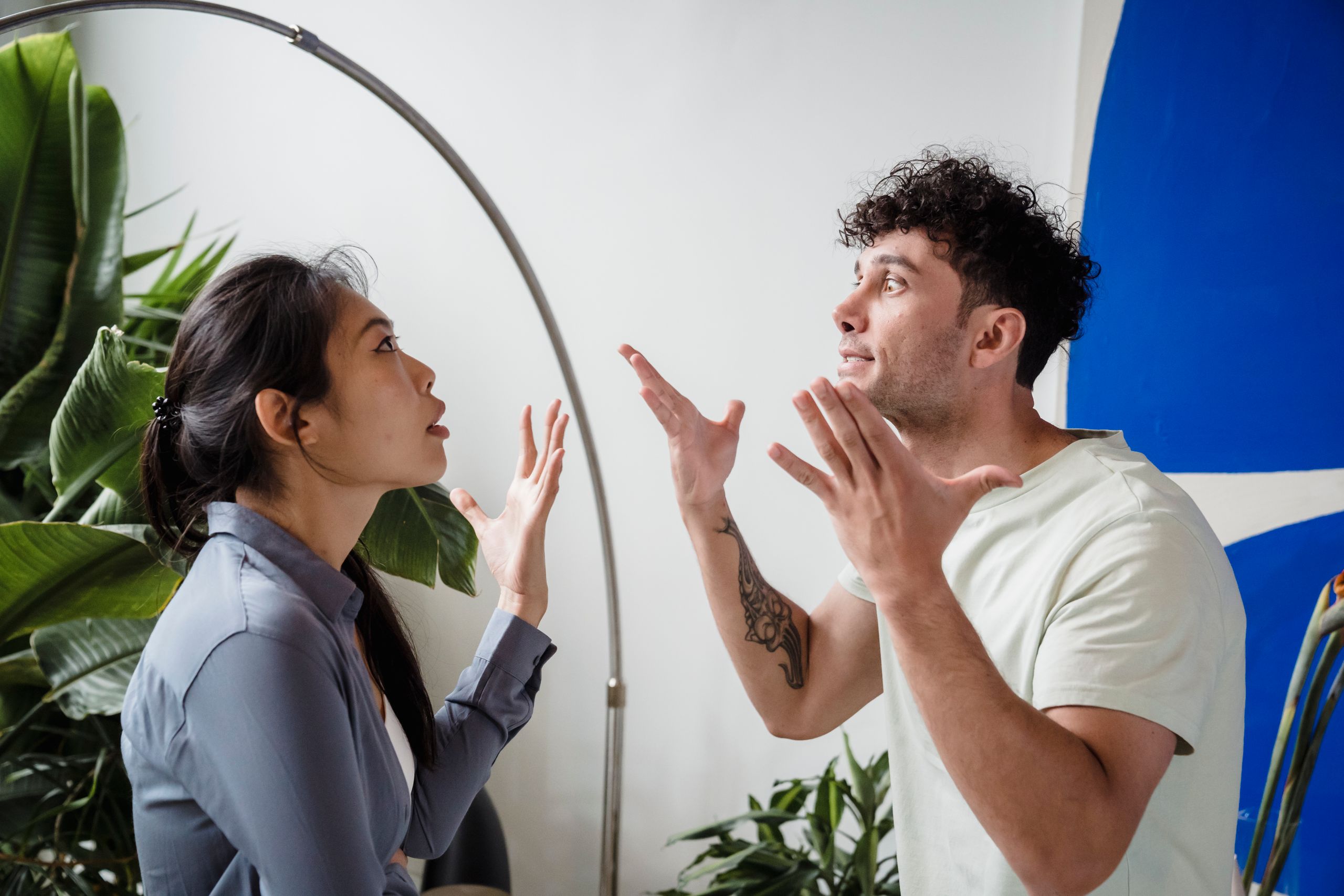A couple argues indoors amidst greenery, showcasing emotions and interpersonal conflict.