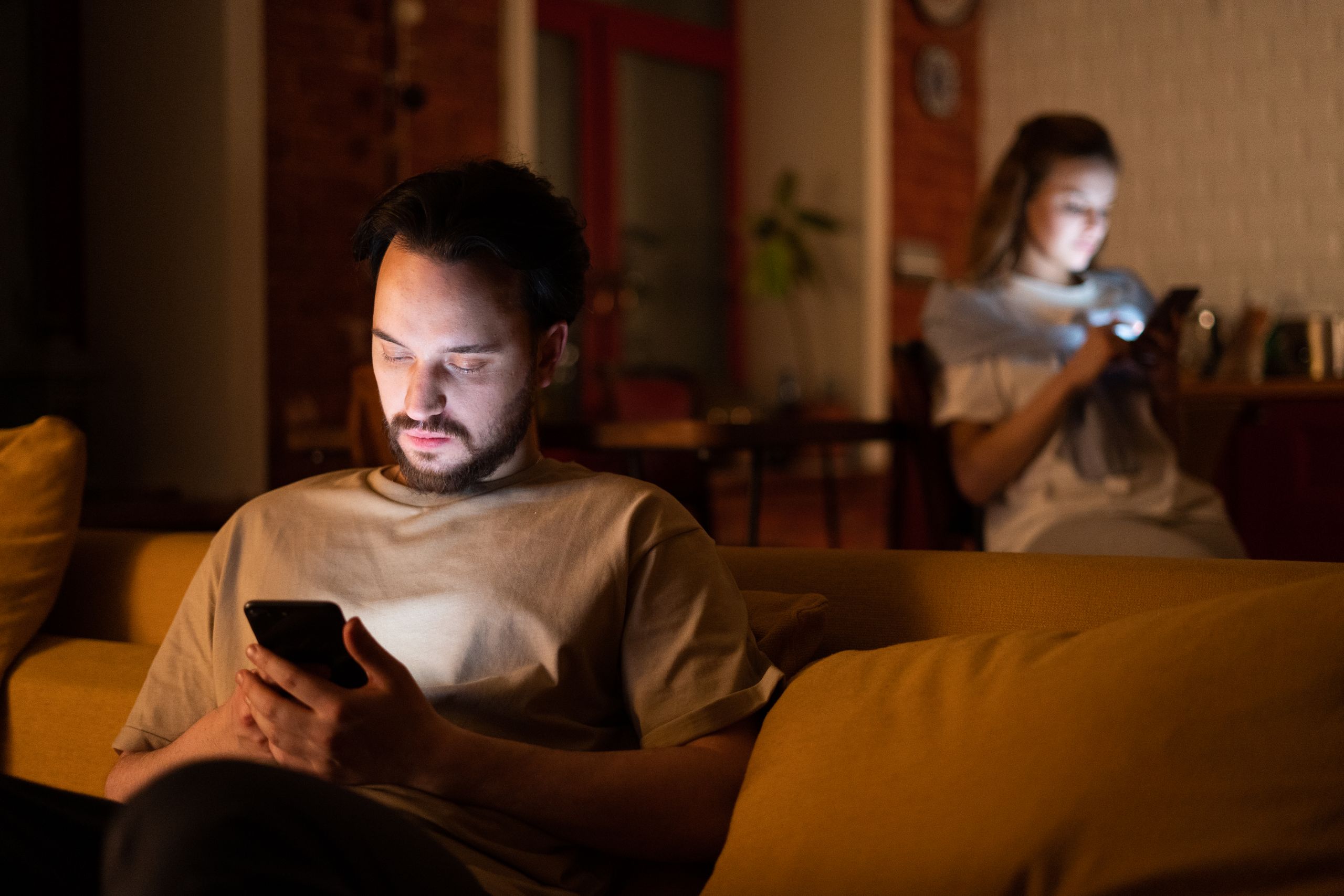 A couple enjoying a cozy evening in a warm home, both using smartphones.