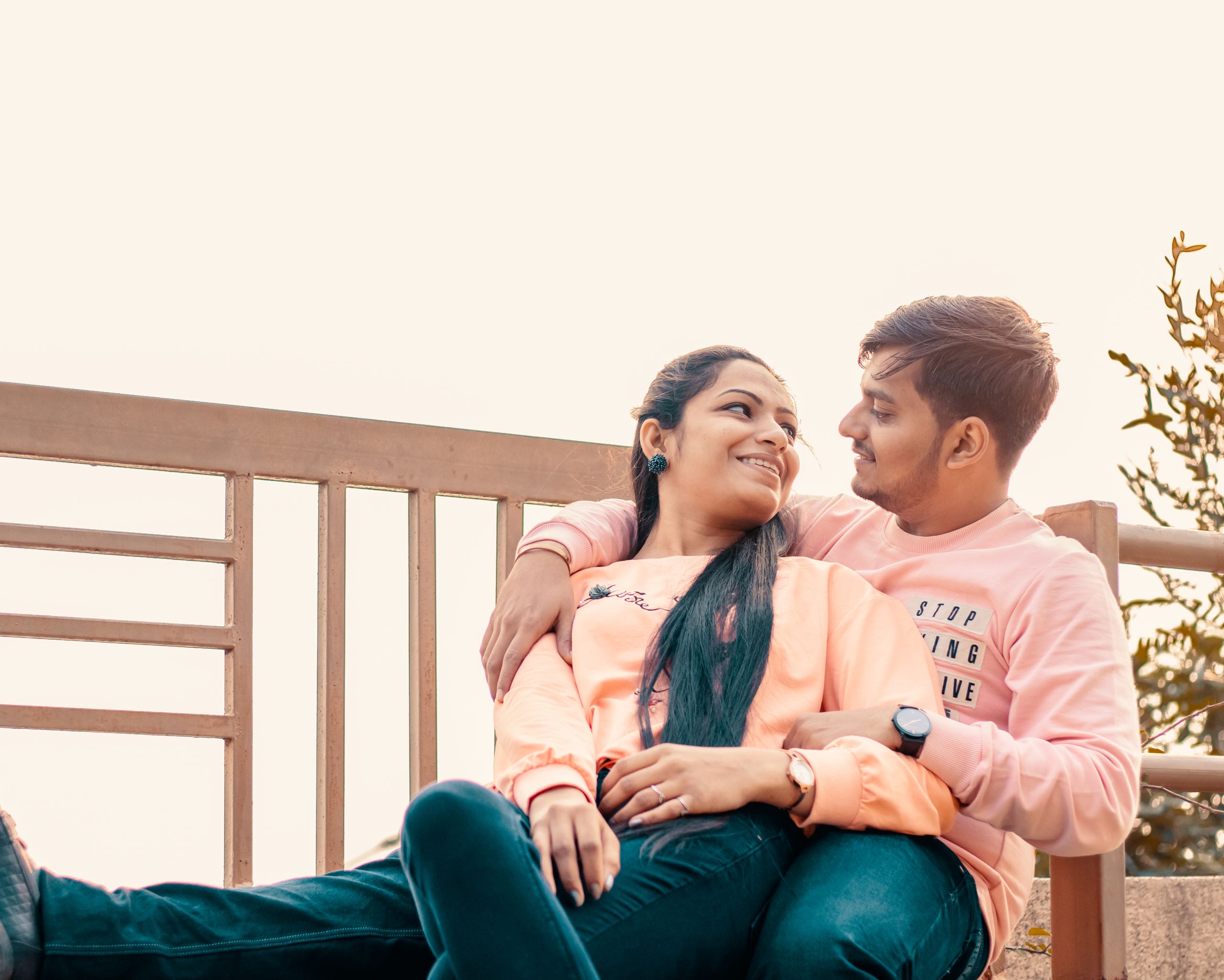 A couple enjoying a sunny day outdoors, sitting on a bench with affection.