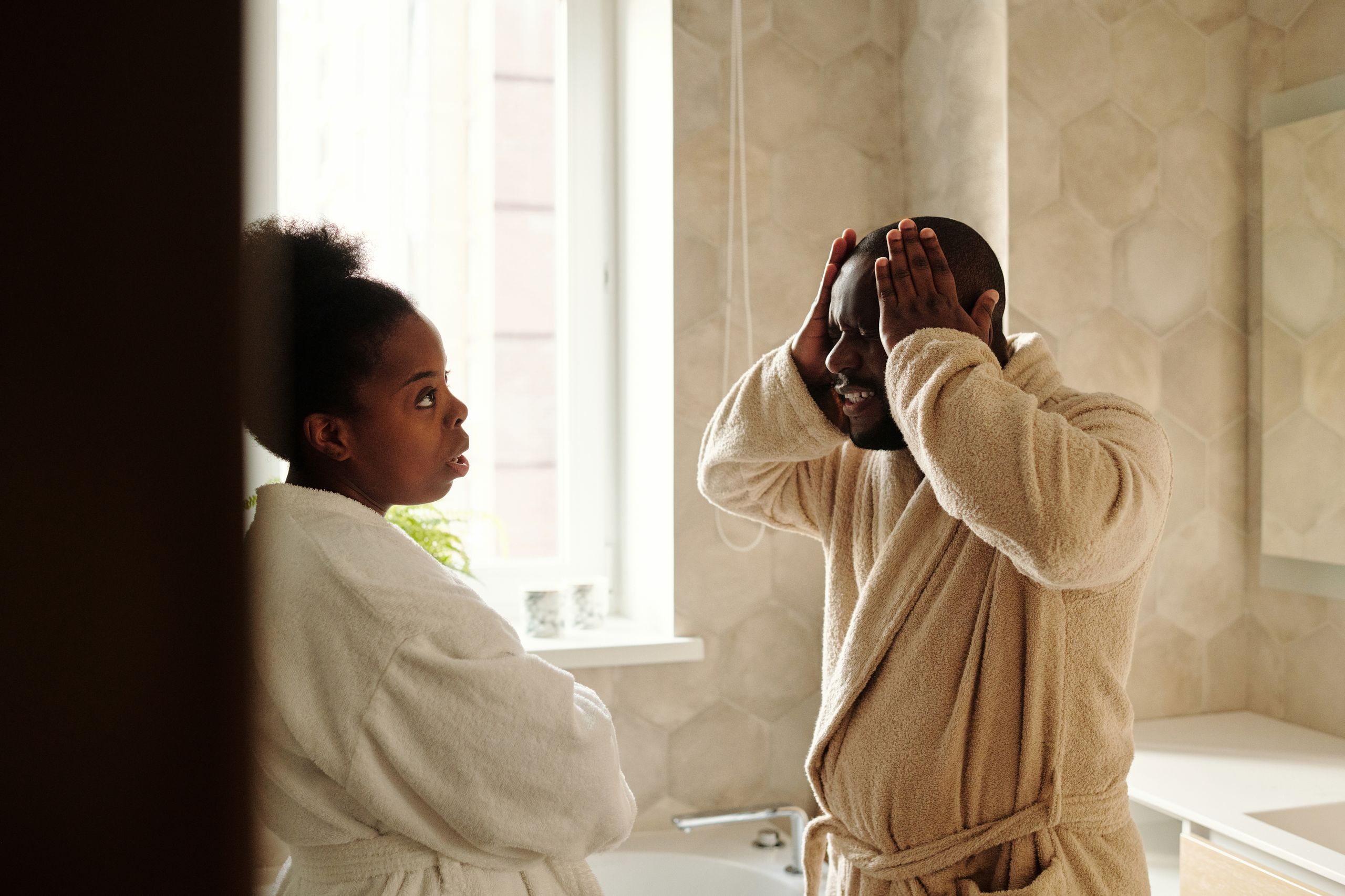 A couple having an emotional conversation in a bathroom setting, wearing robes.