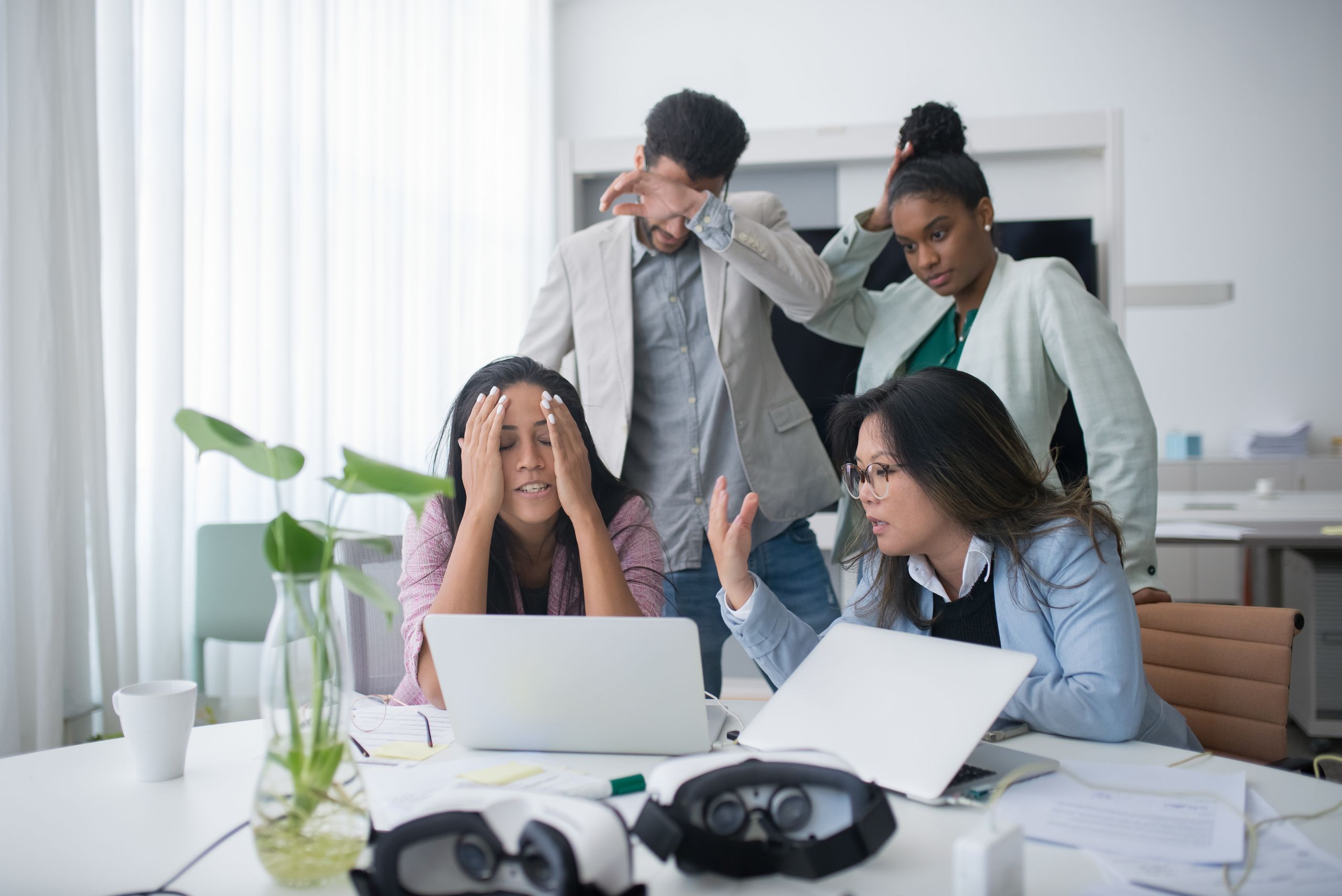 A diverse group of coworkers appearing stressed while working in a modern office meeting room.