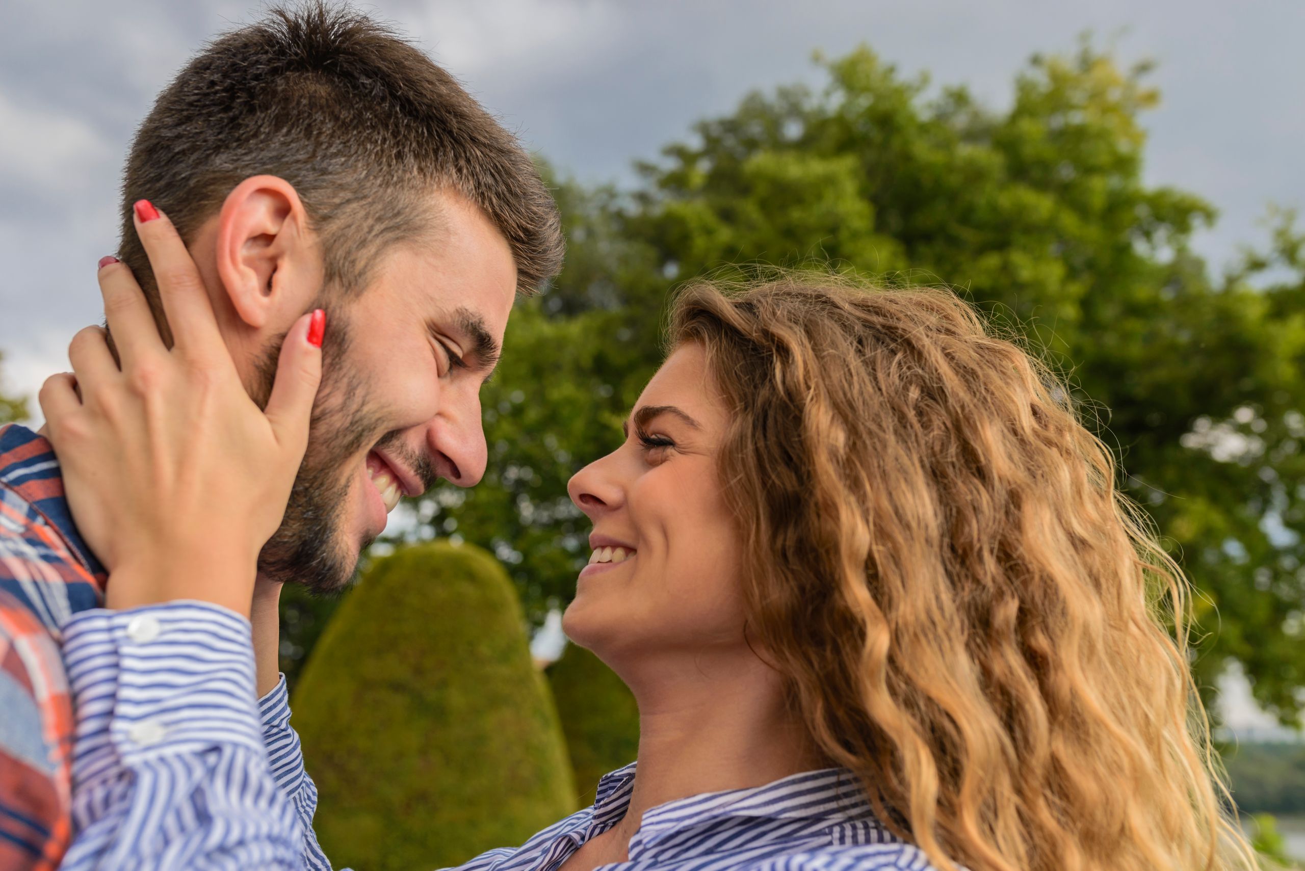 A joyful young couple shares an intimate moment outdoors in a vibrant, green park setting.