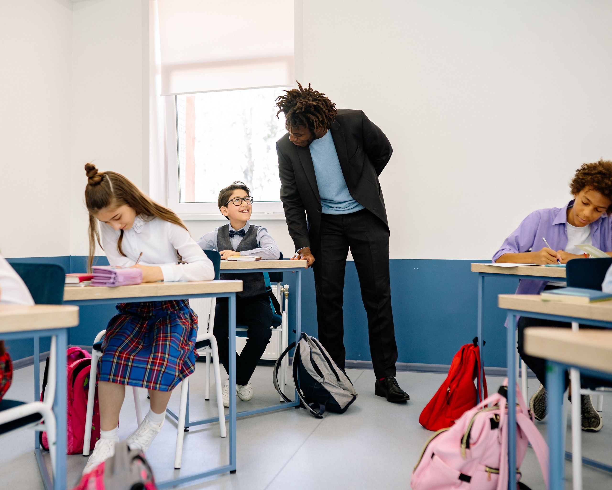 A teacher interacts with students in a bright classroom, promoting a positive learning environment.
