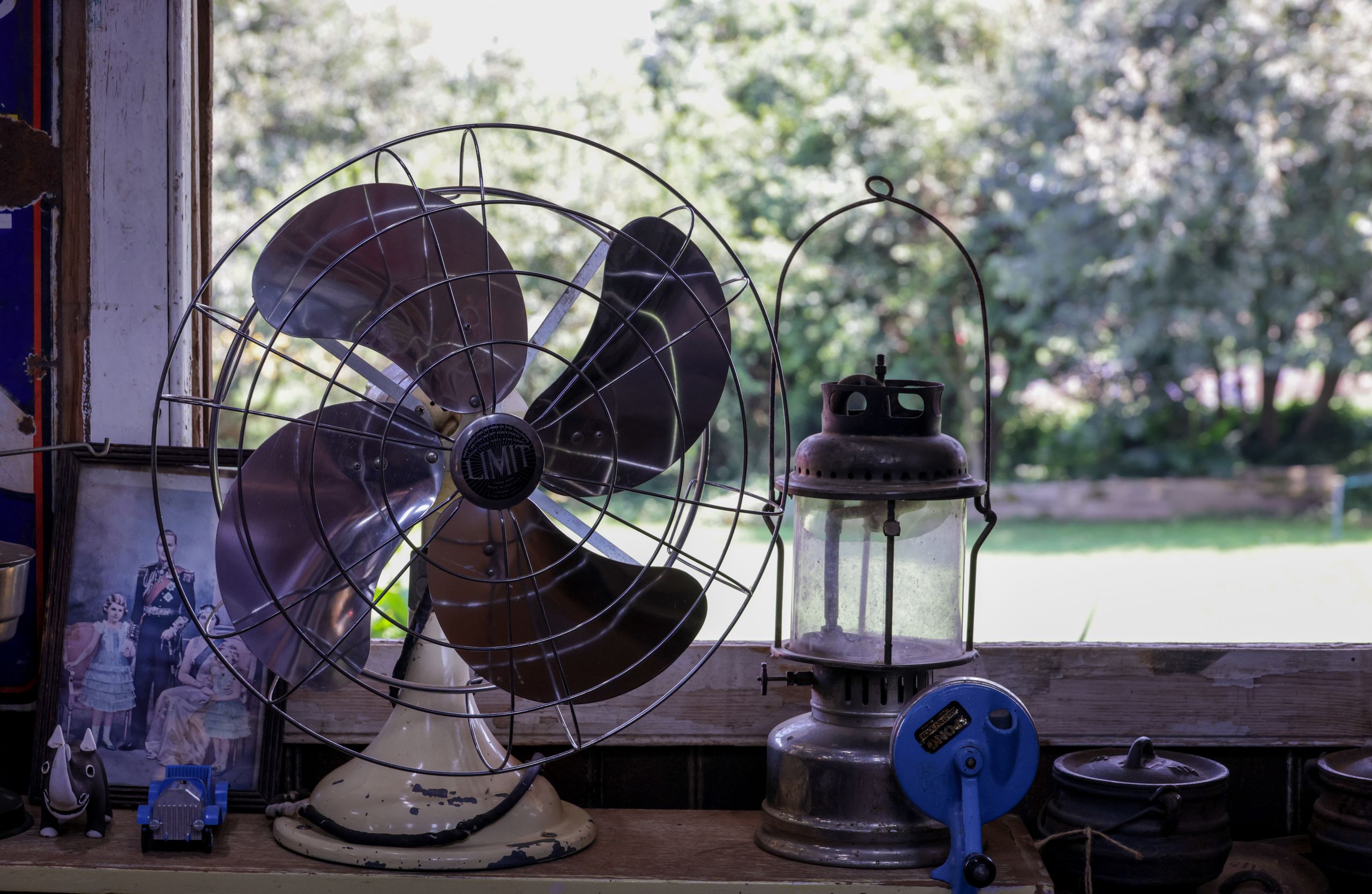 A vintage fan and lantern on a wooden shelf with a picturesque outdoor view.