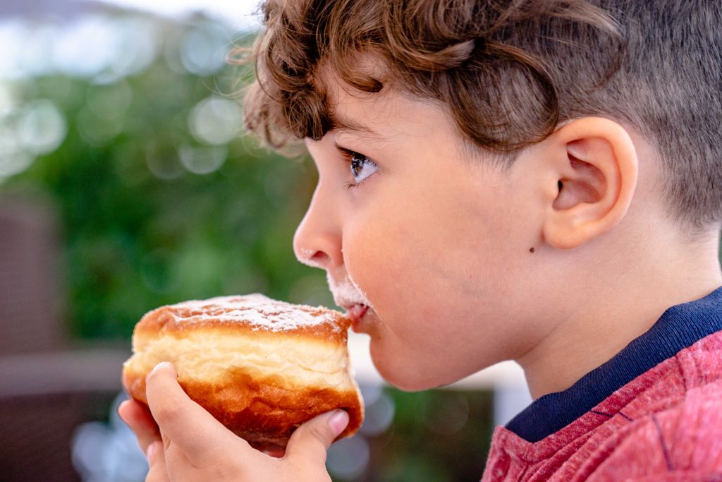 Close-up of a young child savoring a doughnut with powdered sugar outdoors.