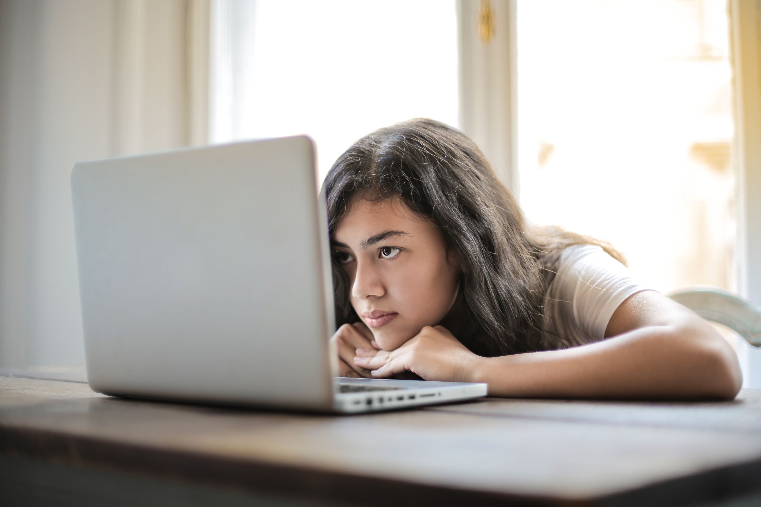 Concentrated bored female sitting against laptop and thoughtfully looking at monitor in sunny day