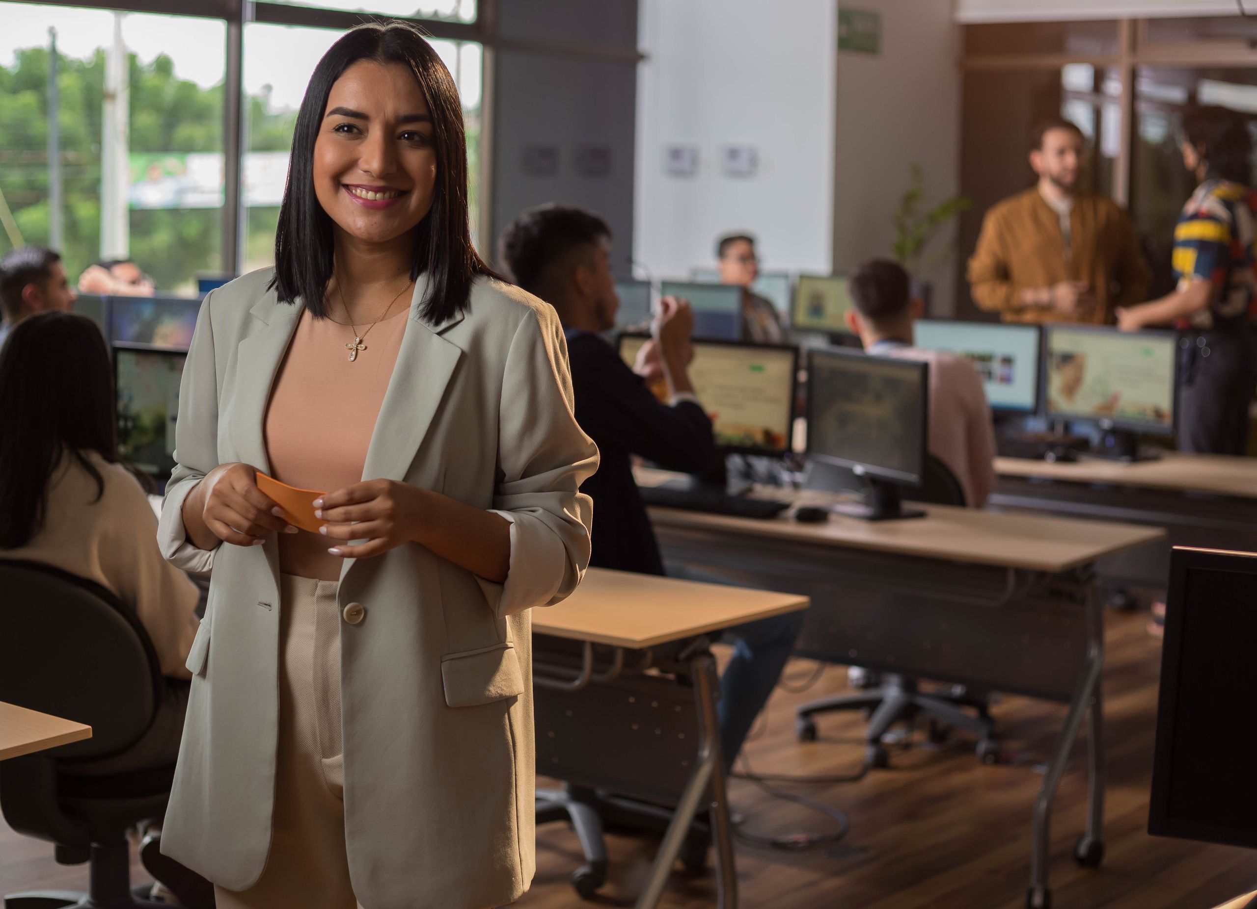 Confident woman smiling in a modern office setting with colleagues working in the background.