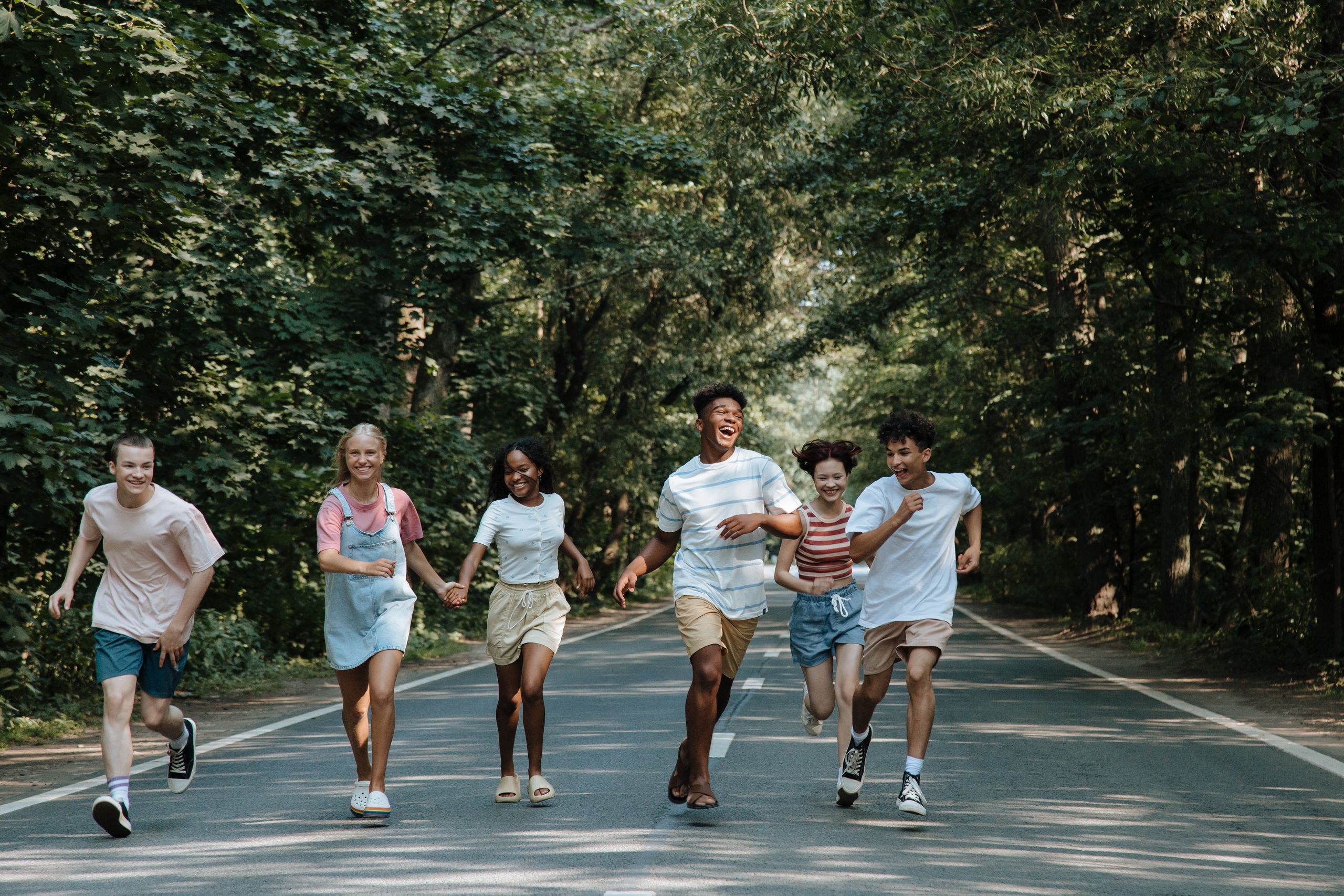 Group of joyful teenagers running and laughing on a forest road during summer.
