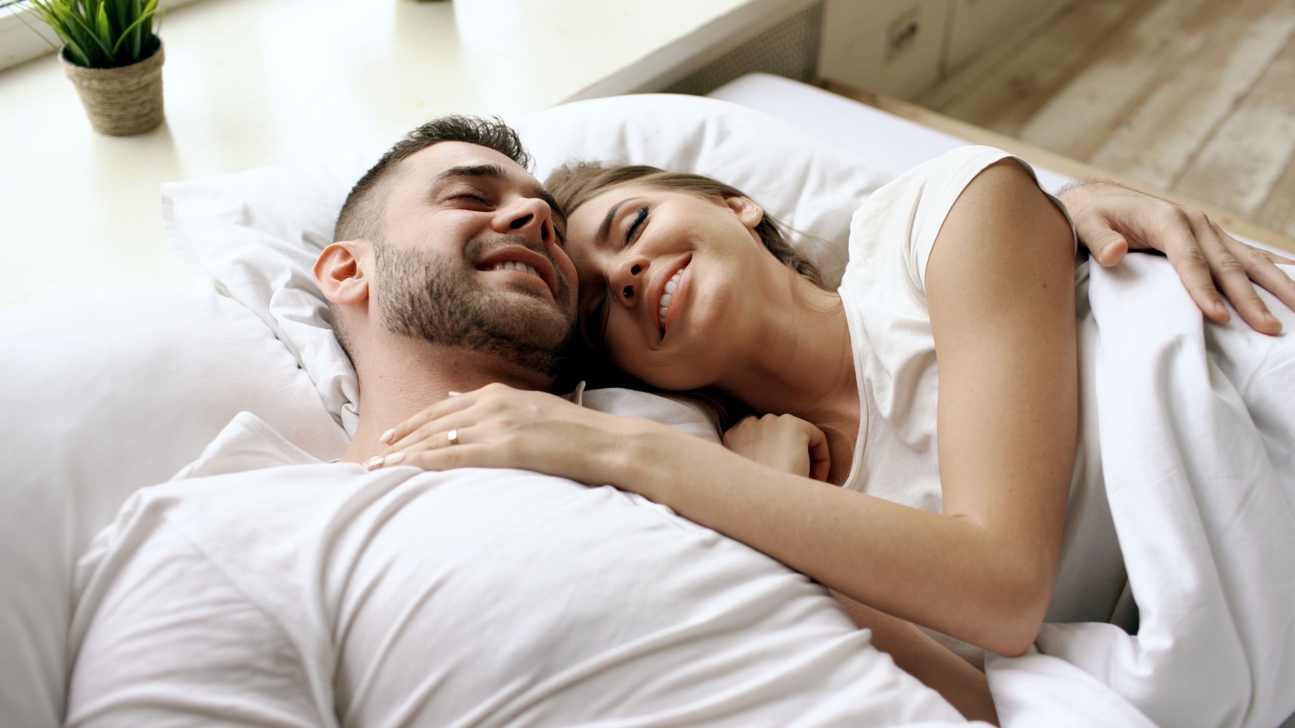 Joyful couple cuddling in bed, enjoying a peaceful morning indoors.