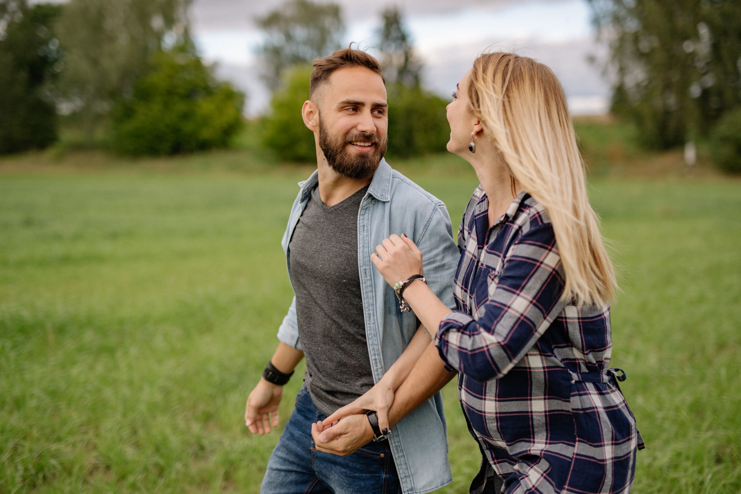 Smiling couple walking hand in hand across a green field, sharing a joyful moment.