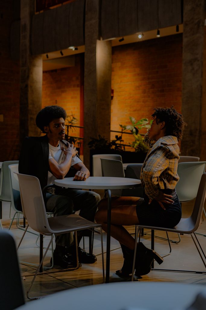 Two young adults engaged in a cozy chat at a modern cafe with warm lighting.
