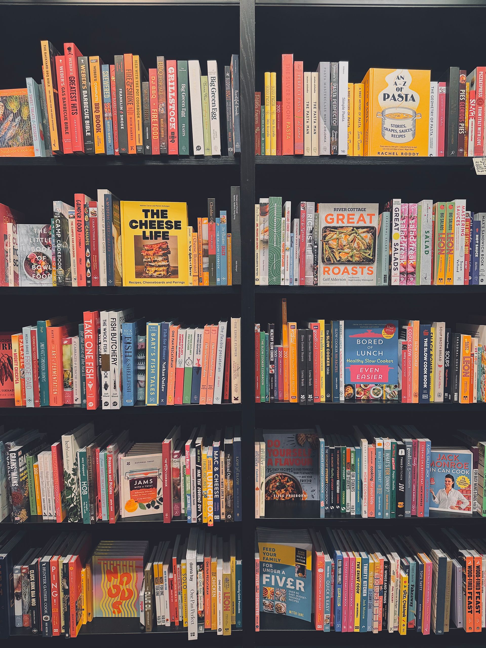 Vibrant array of cookbooks displayed on black shelves, showcasing culinary diversity.