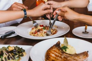 Close up of group of friends hands with a fork having fun eating and having italian dinner together