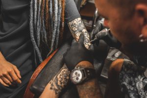 girl with dreadlocks in a tattoo parlor. The master creates a picture on the body of a young beautiful girl. Close-up of hands and tattoo machine